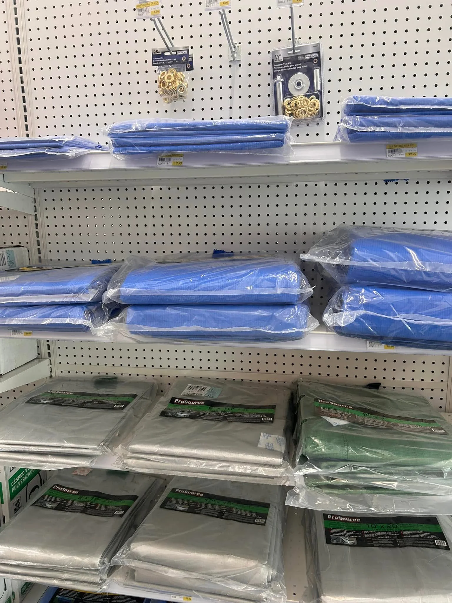 Store shelf with packaged green and white tarp or plastic sheeting, next to a shelf with blue tarps and various hardware items like washers and tool kits.