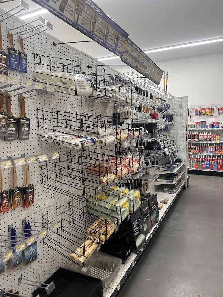 Empty retail shelf with various hooks and empty grid spaces, located in a store aisle with several products on the right wall.
