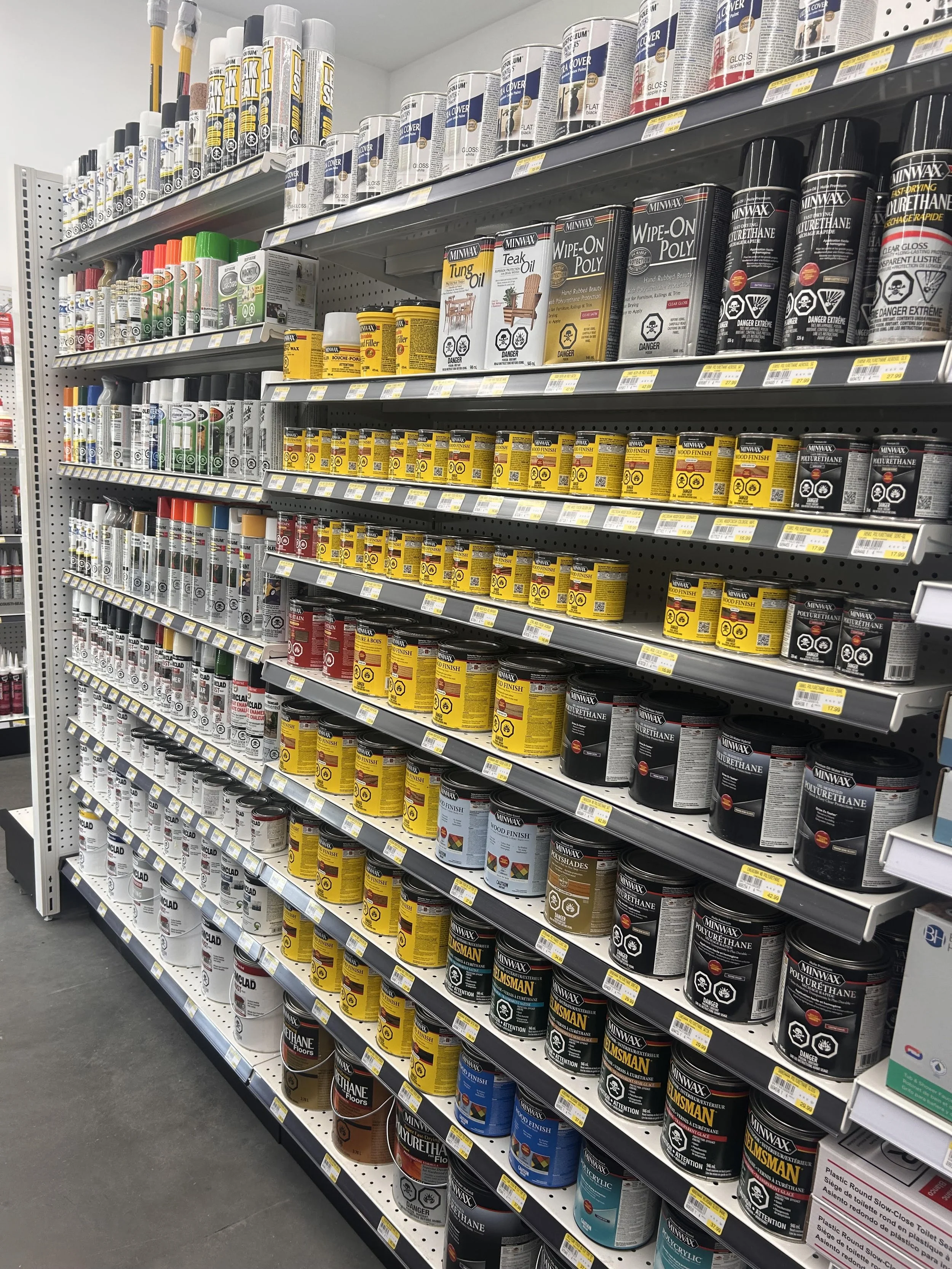 Aisle of store shelves with cans of paint and painting supplies, in a hardware store.
