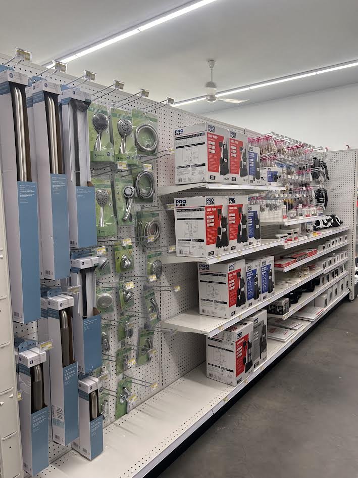 Store aisle with bathroom fixtures and accessories, including showerheads, shower rods, and pumps on shelves.