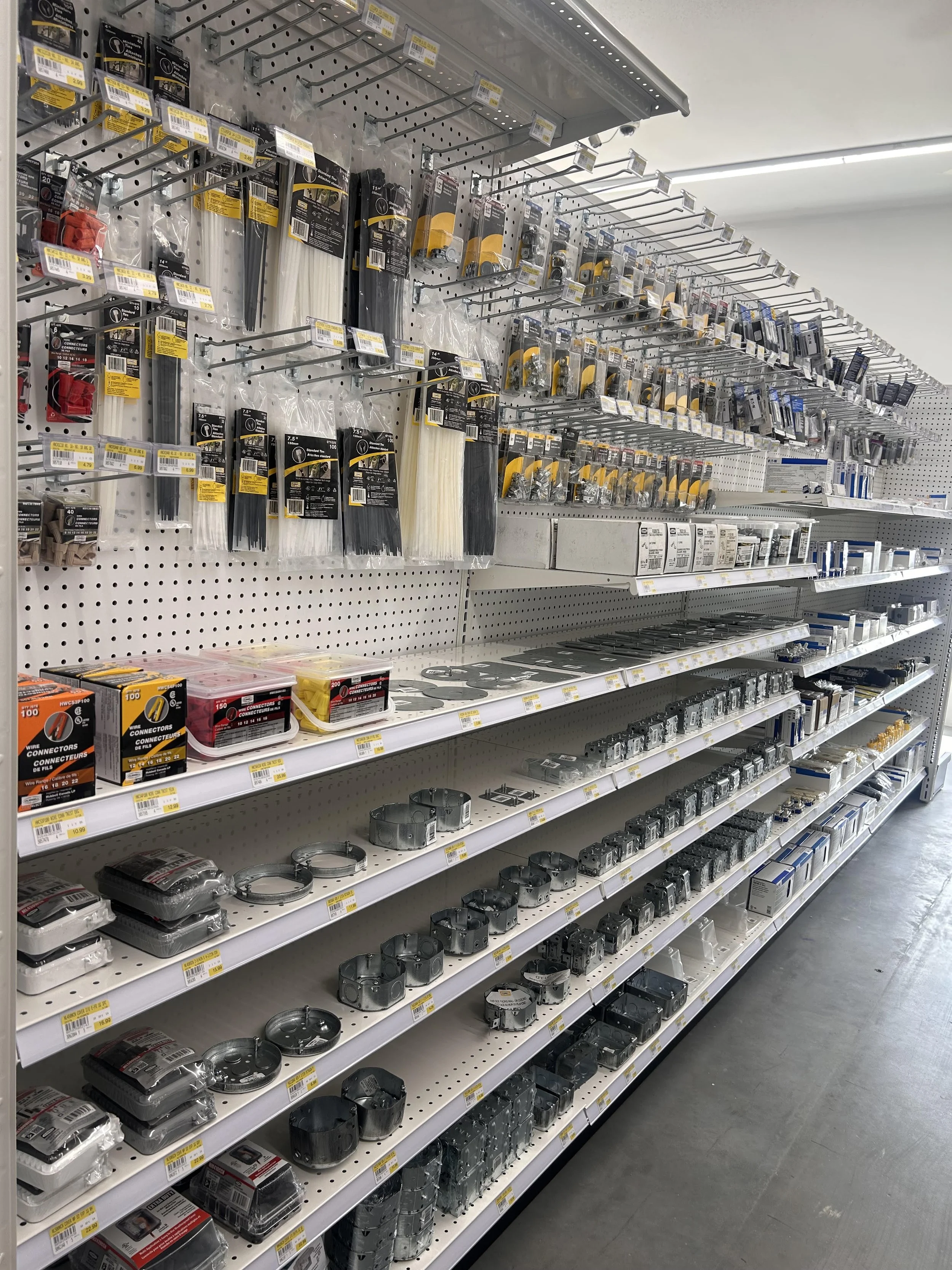 Retail store aisle displaying various electrical components such as wire connectors, terminal blocks, and junction boxes on white shelving units.