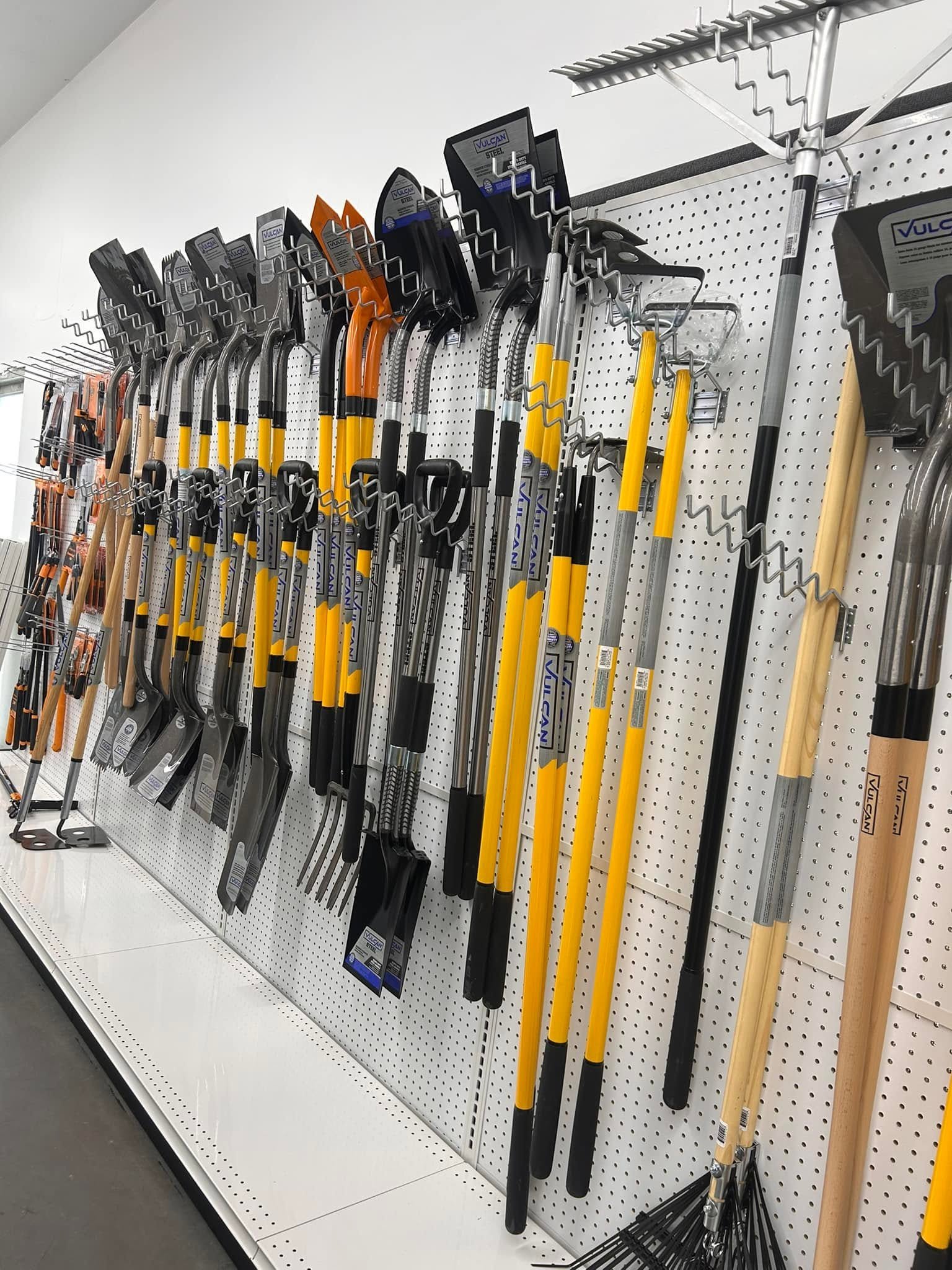 A display of various garden tools, including shovels, rakes, and hoes, hung on a pegboard in a hardware store.