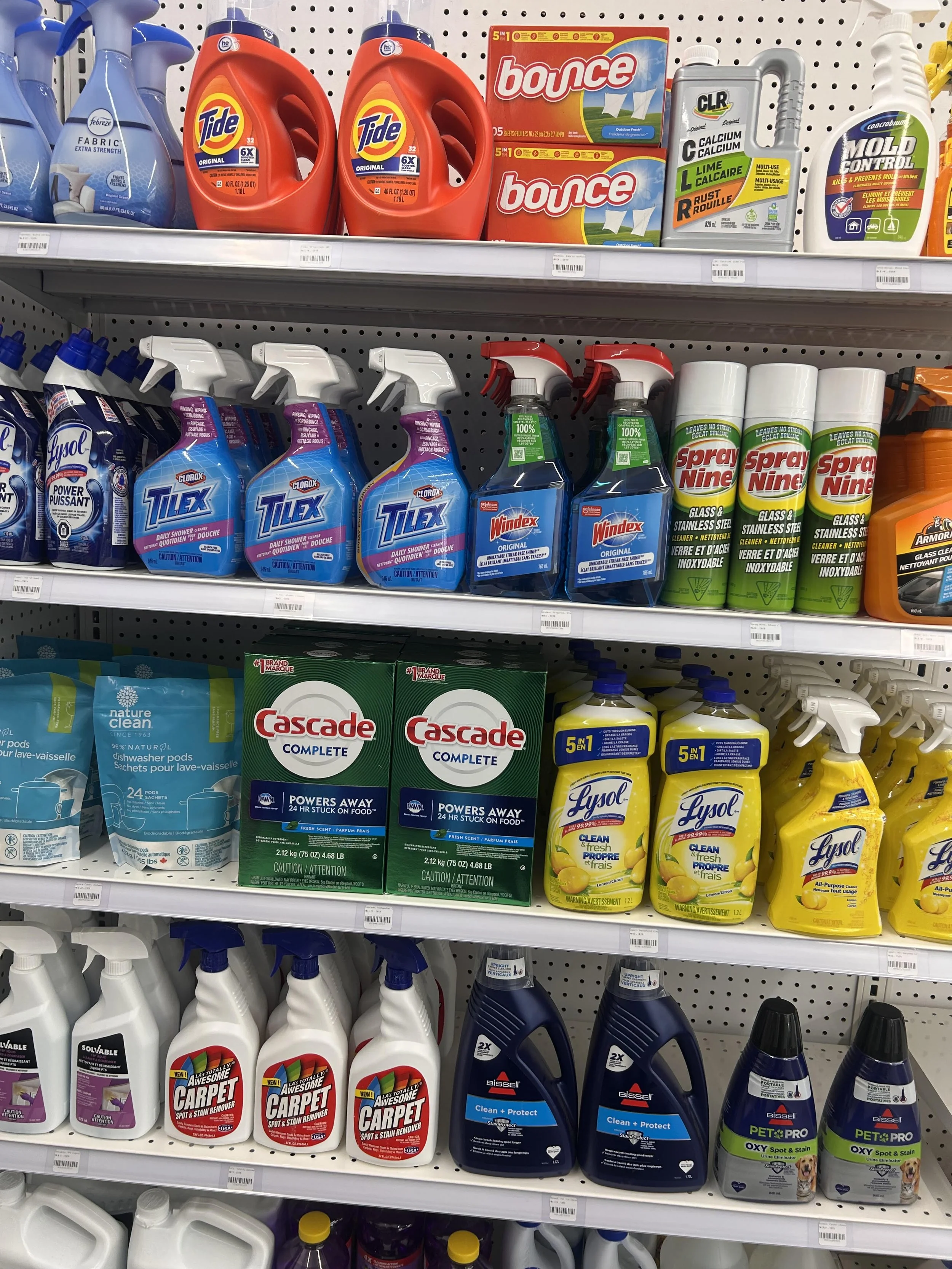 Shelf display of laundry and cleaning products, including Tide detergent, Bounce fabric softener sheets, CLR calcium lime rust remover, Lysol disinfectant spray, and carpet stain remover, among other cleaning supplies.