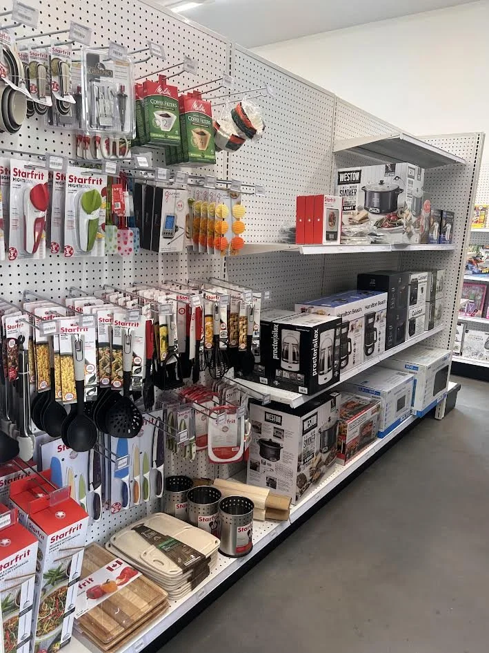 Kitchen utensils and gadgets displayed for sale on a store shelf, including spatulas, measuring cups, a rice cooker, and cooking knives.