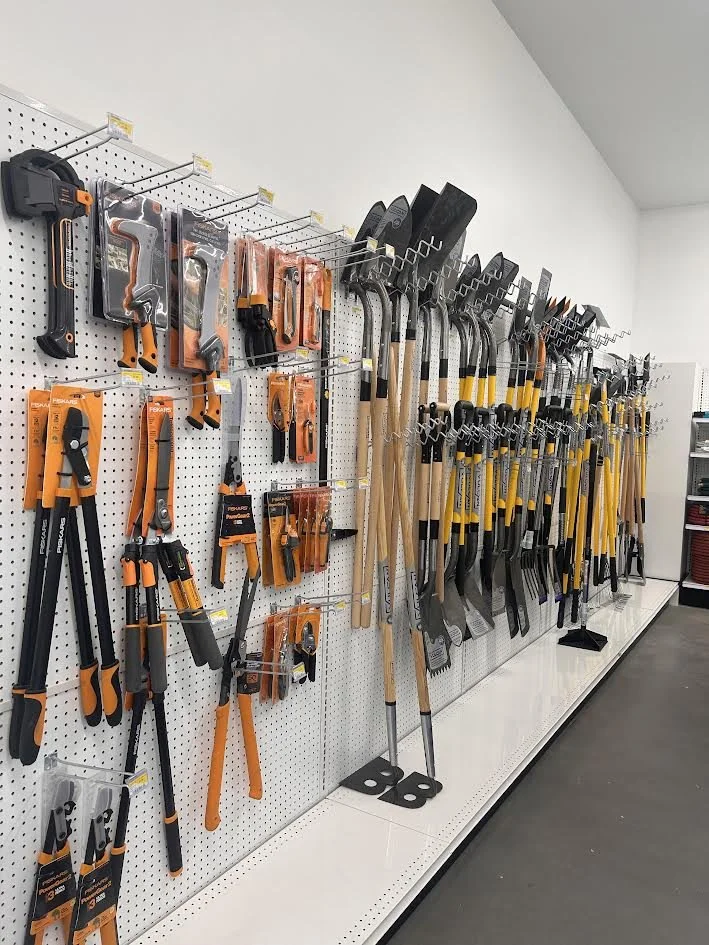 A display of various hand tools including hammers, saws, pruners, and axe heads arranged on a pegboard in a store.