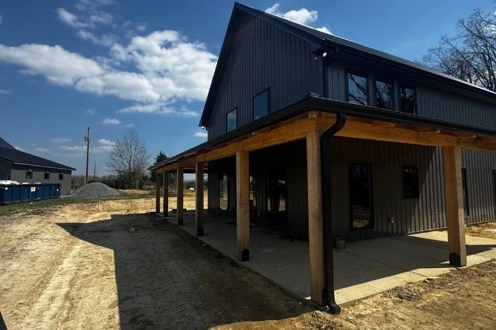 Two-story dark gray metal home with black seamless gutters and a timber frame wrap-around porch