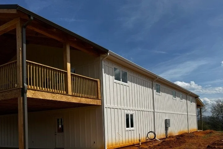 Side view of a two-story building with a porch and white exterior, set against a partly cloudy sky.