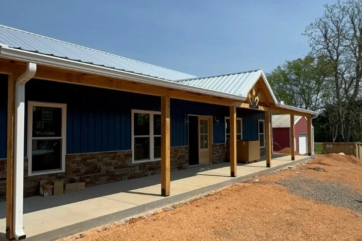 Blue metal home with white seamless gutters, stone veneer base, timber porch columns, and a silver metal roof