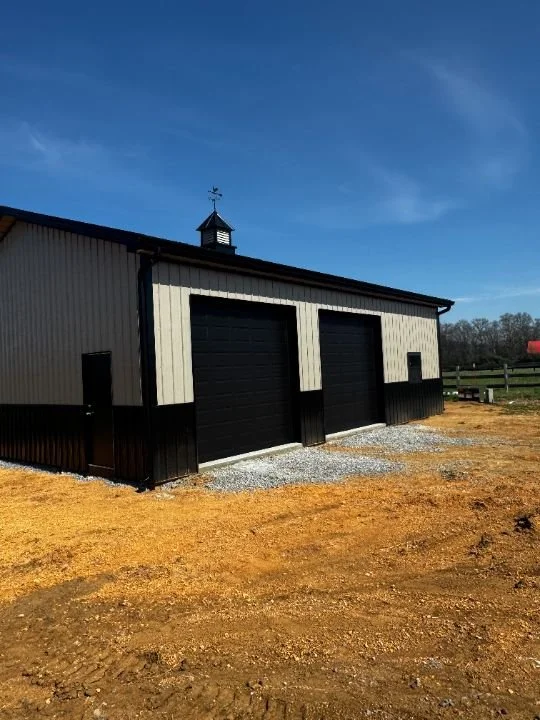 White metal shop building with garage bays and gravel driveway on a farm property
