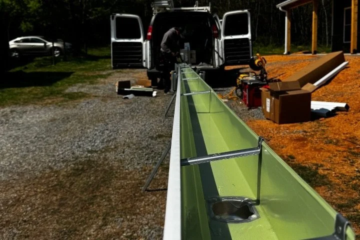 Gutter installer working at the back of a work van fabricating a custom green seamless gutter section with tools and equipment nearby