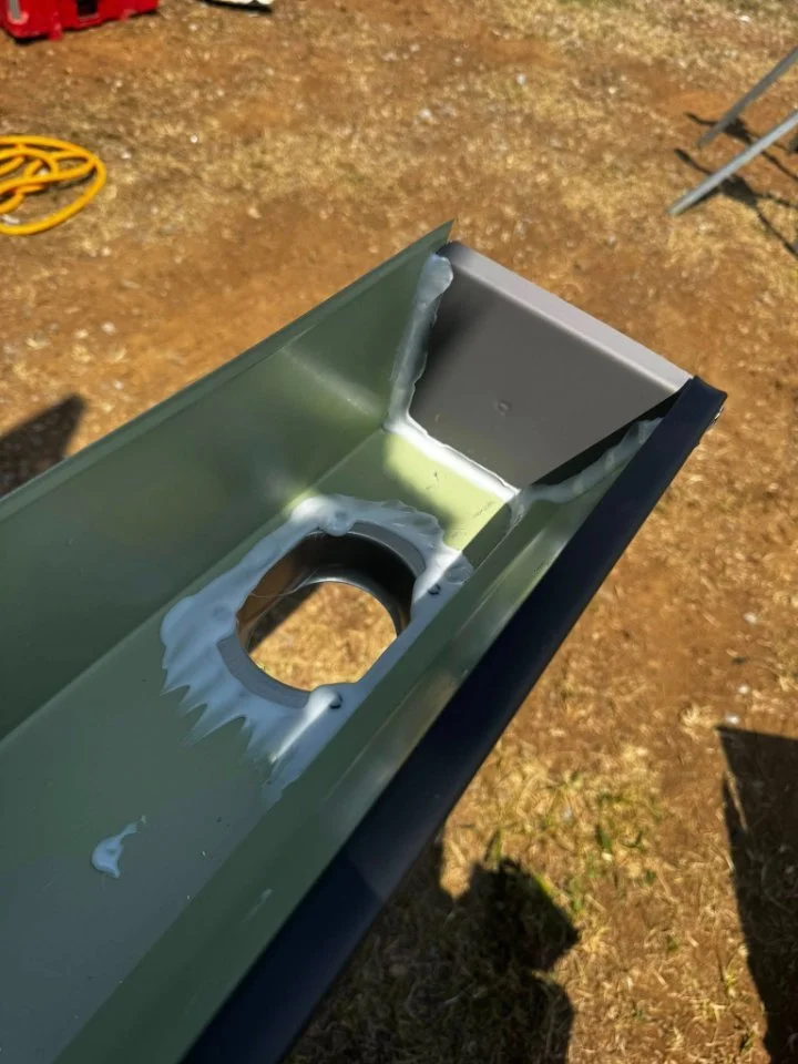 Close-up of a metal piece with a circular hole, welded with some white filler material, on a dirt ground outdoors.