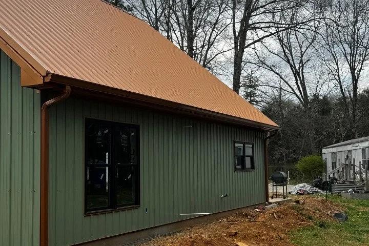 Side view of a green metal building with copper seamless gutters and downspouts along a copper metal roof