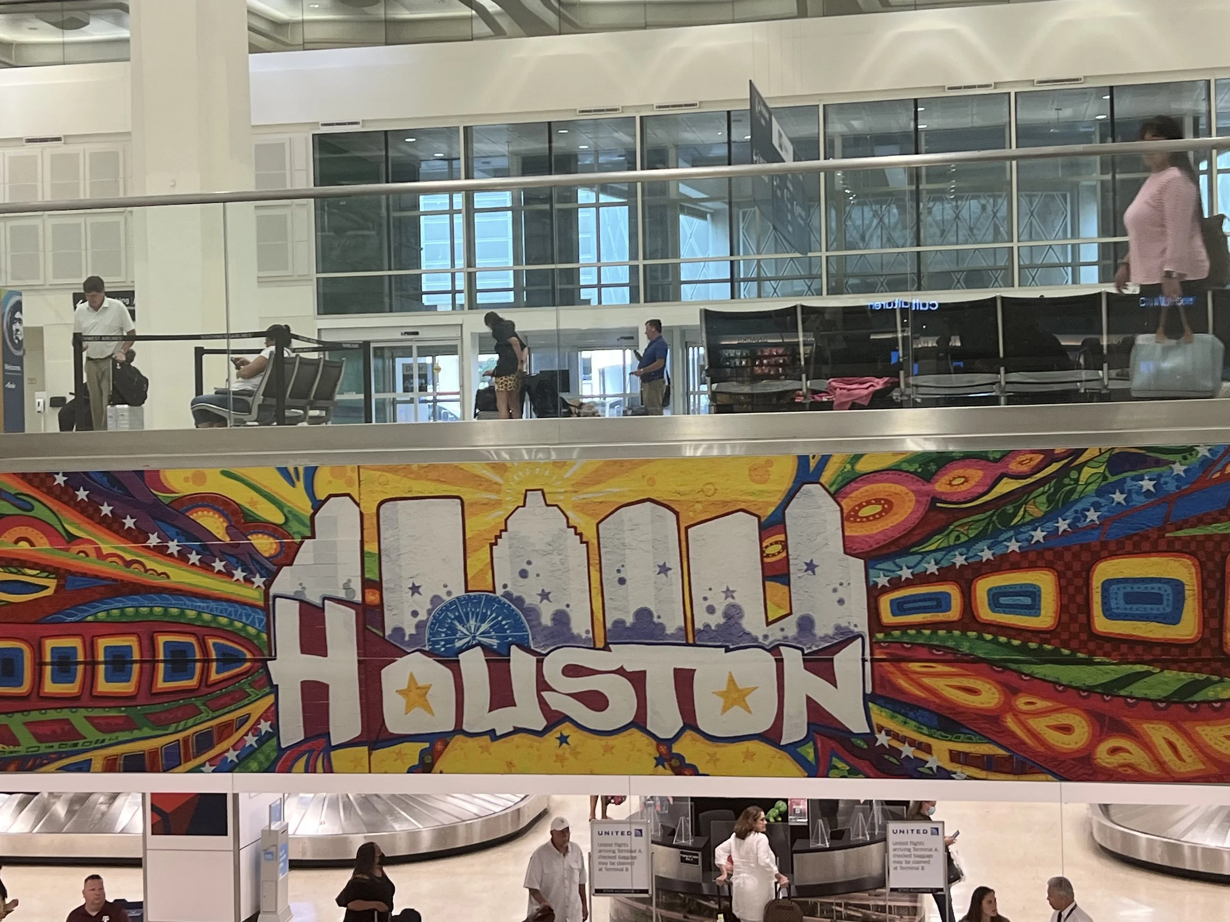 Colorful airport sign featuring the Houston skyline and the word 'Houston' in bold letters with stars, surrounded by vibrant swirling patterns.