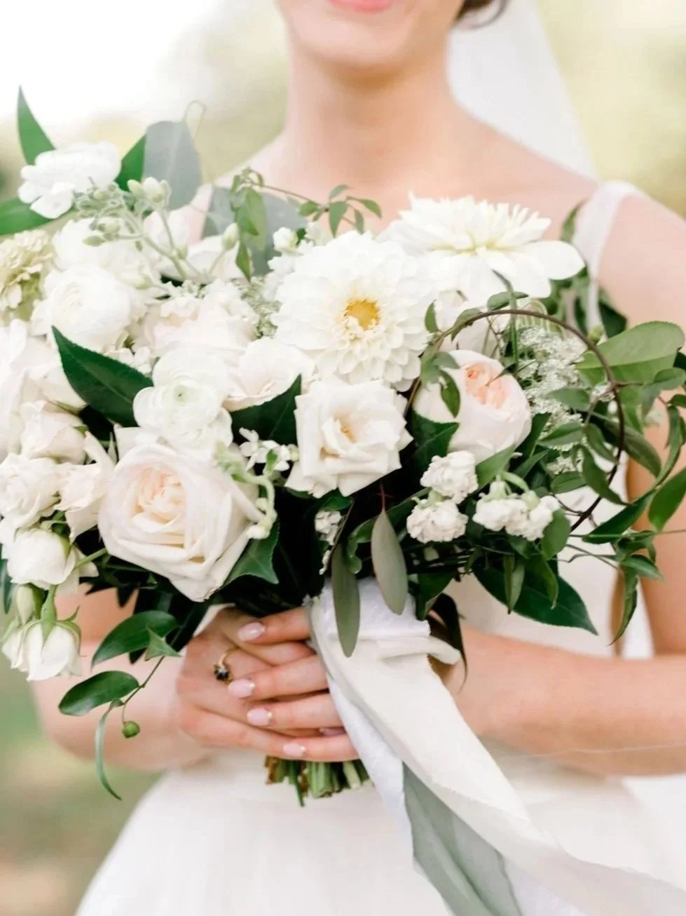 A woman in a white dress holding a large bouquet of white and pale pink flowers, including roses and dahlias.