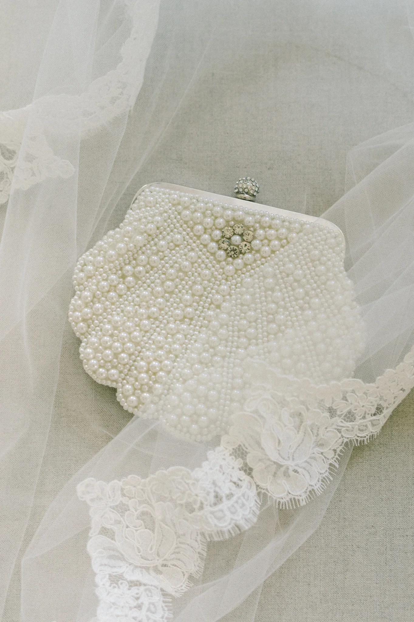 Elegant white wedding clutch adorned with pearls and rhinestones, resting on delicate lace fabric.