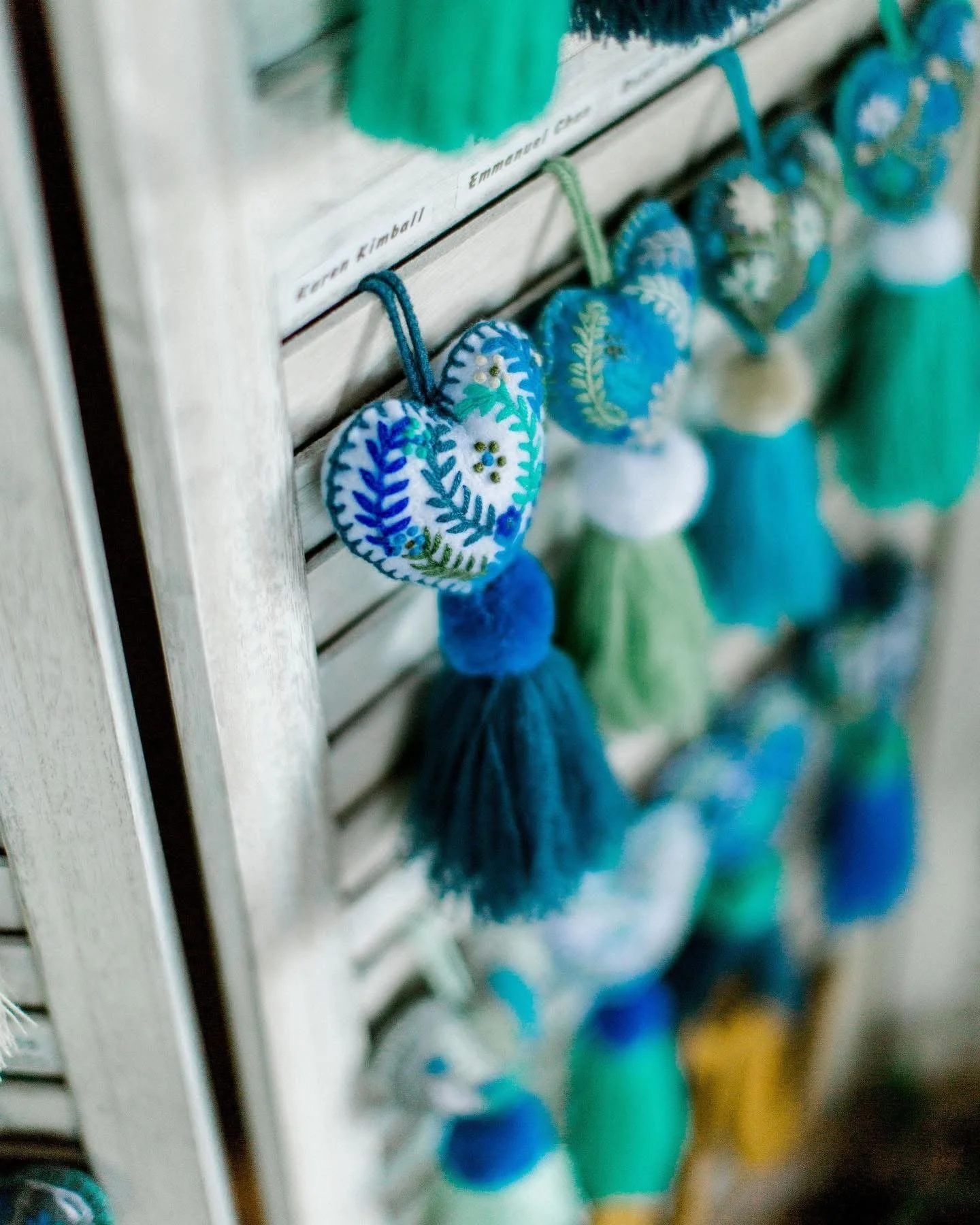 Colorful felted wool ornaments shaped like hearts and teardrops, hanging with string clips on a wooden slat.