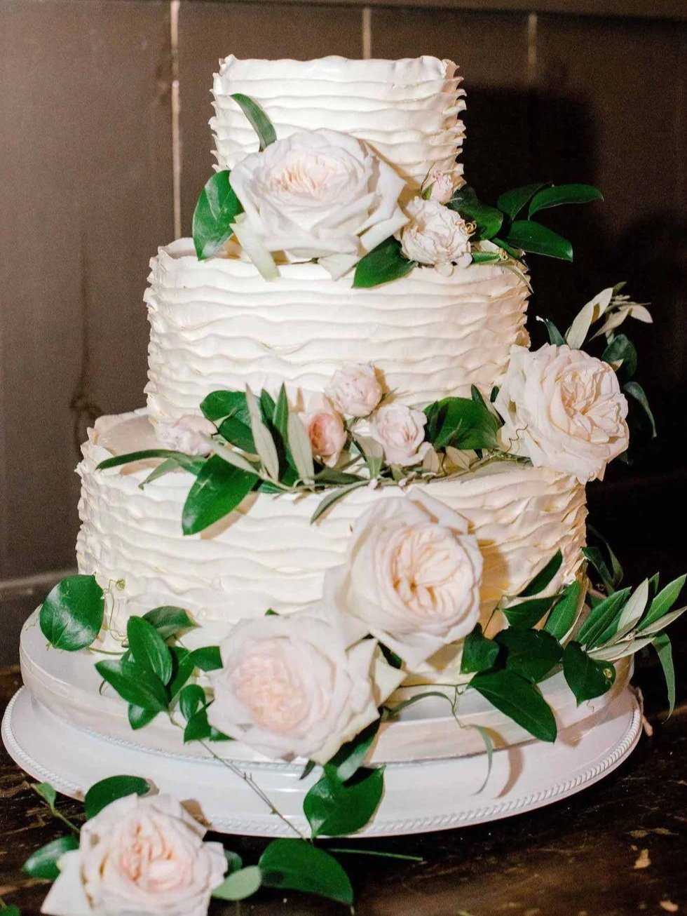 A three-tier wedding cake decorated with white and blush roses and green leaves.