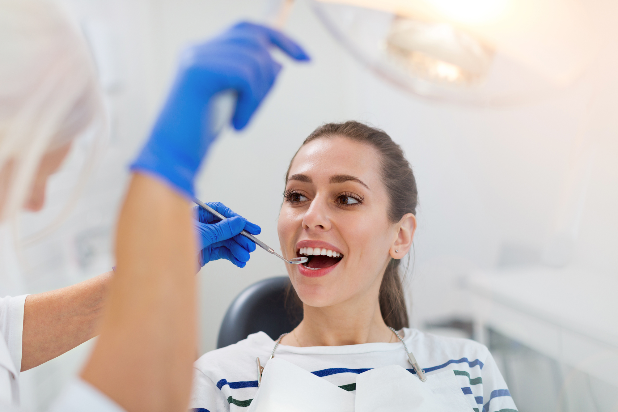 A woman at a dental appointment is smiling as a dentist in gloves uses a dental tool in her mouth.