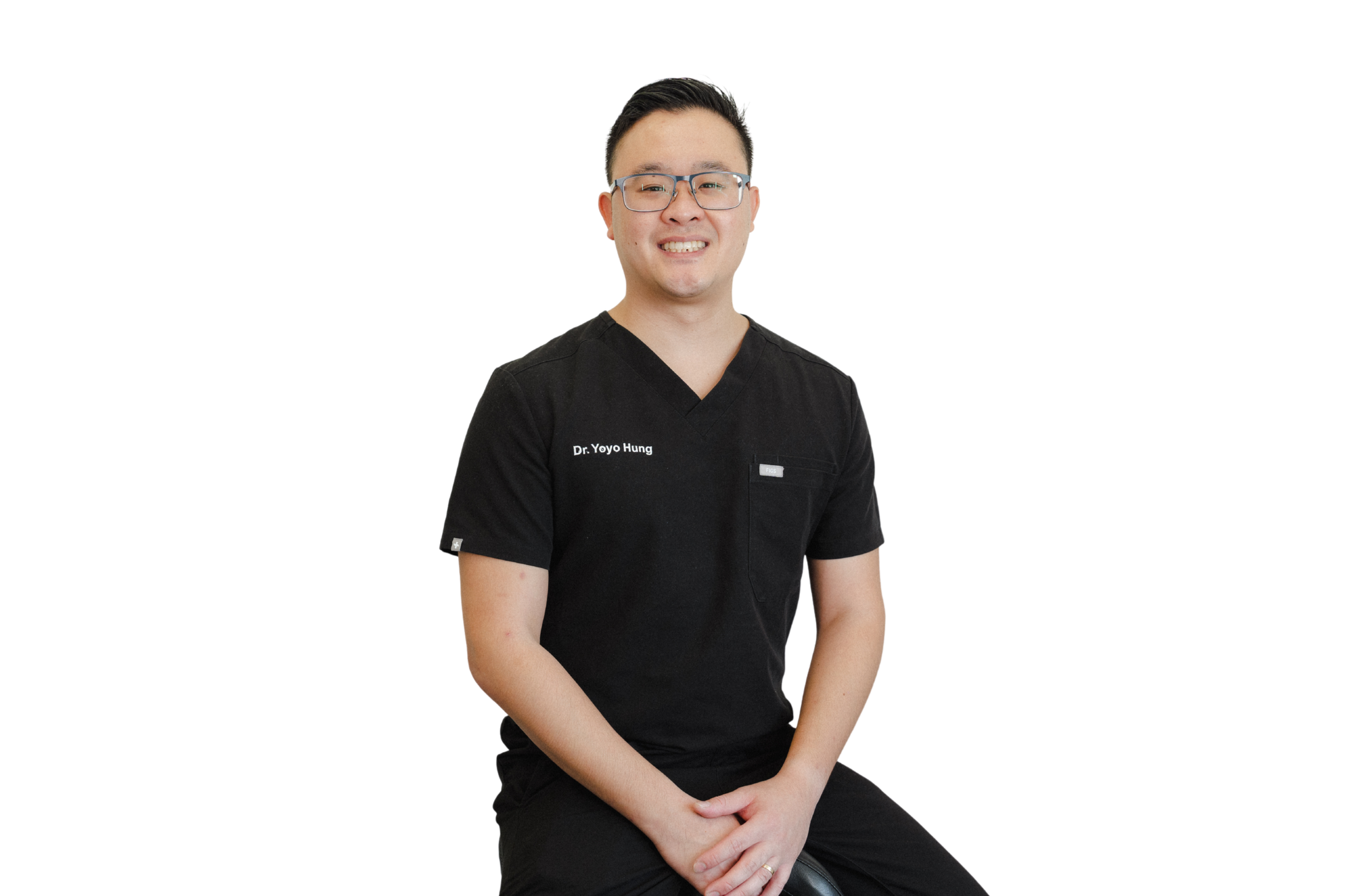 Portrait of a male healthcare professional wearing black scrubs with 'Dr. Yoyo Hung' embroidered, sitting on a stool against a white background, smiling at the camera.