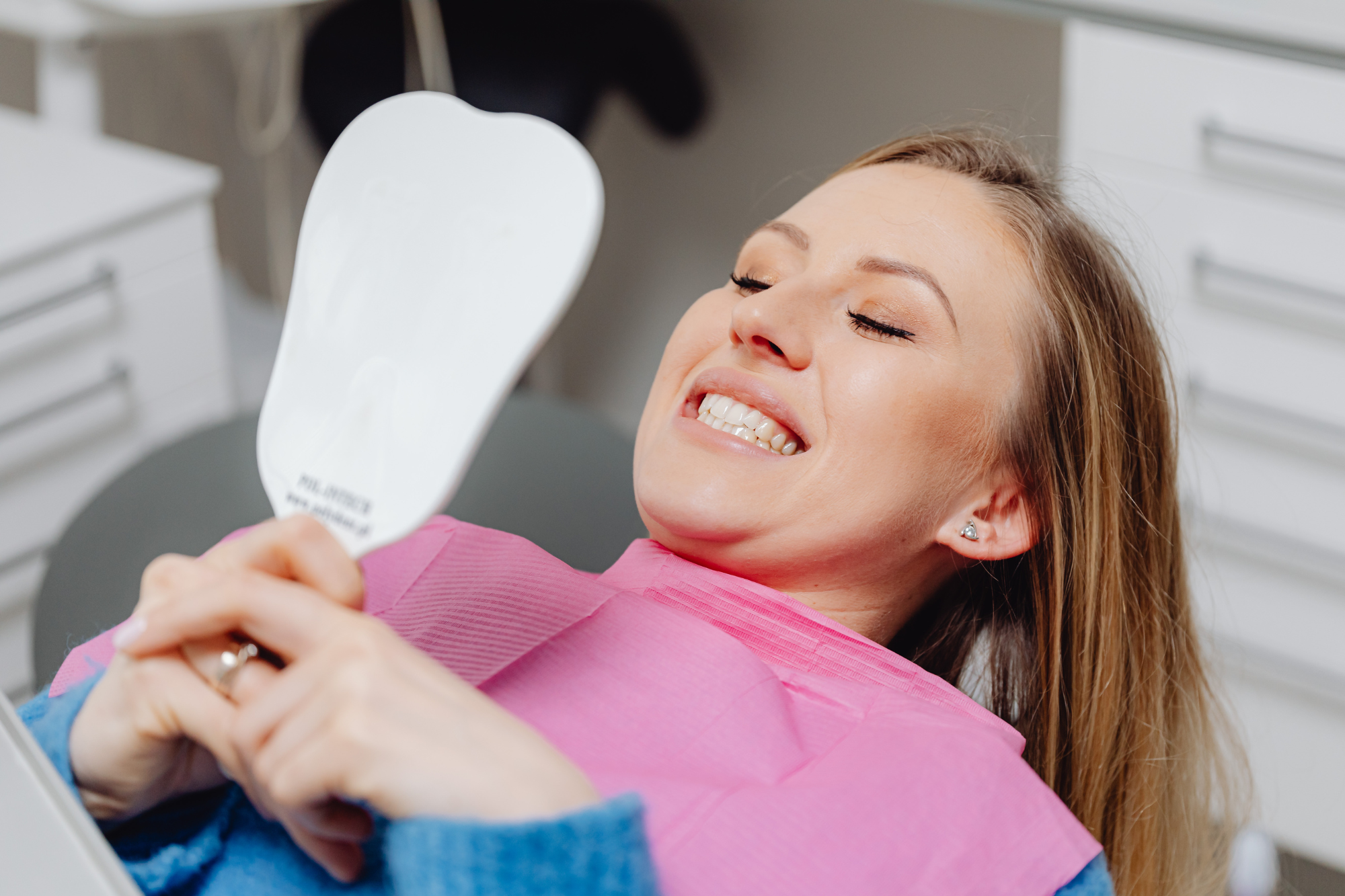 Woman sitting in dental chair smiling and looking at a mirror.