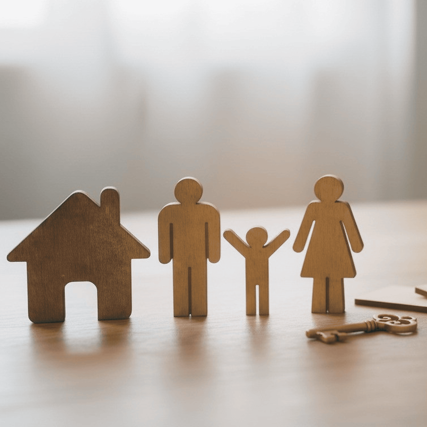 Wooden figures of a house, man, child, and woman standing on a wooden surface with a pair of keys nearby.