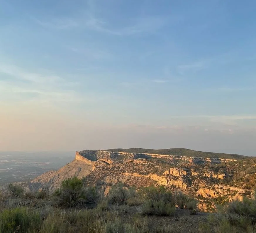 A rocky plateau with steep cliffs overlooking a flat landscape under a blue sky with wispy clouds.