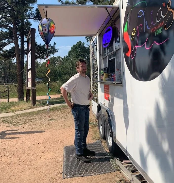 Man standing at a Mexican food food truck on a sunny day.