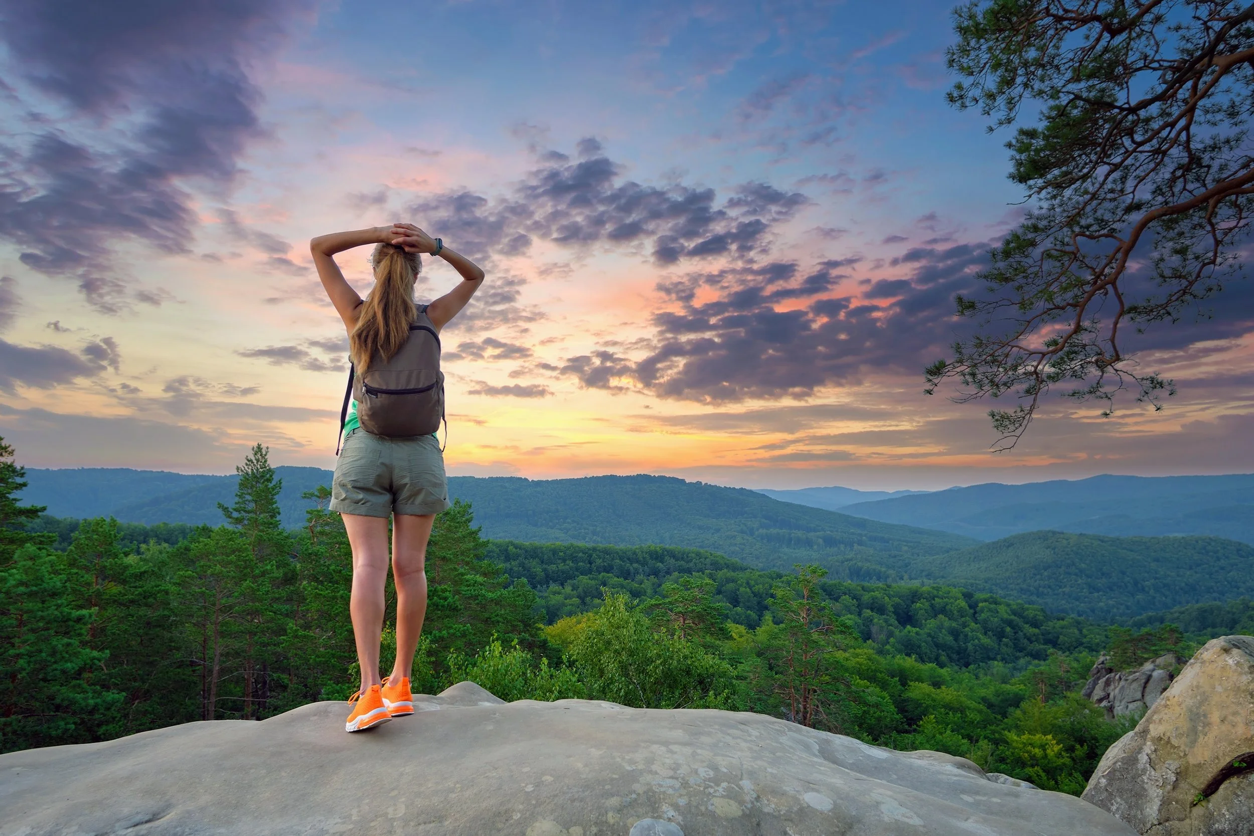 Person standing on a mountain overlook at sunset, representing perspective, clarity, and moving forward