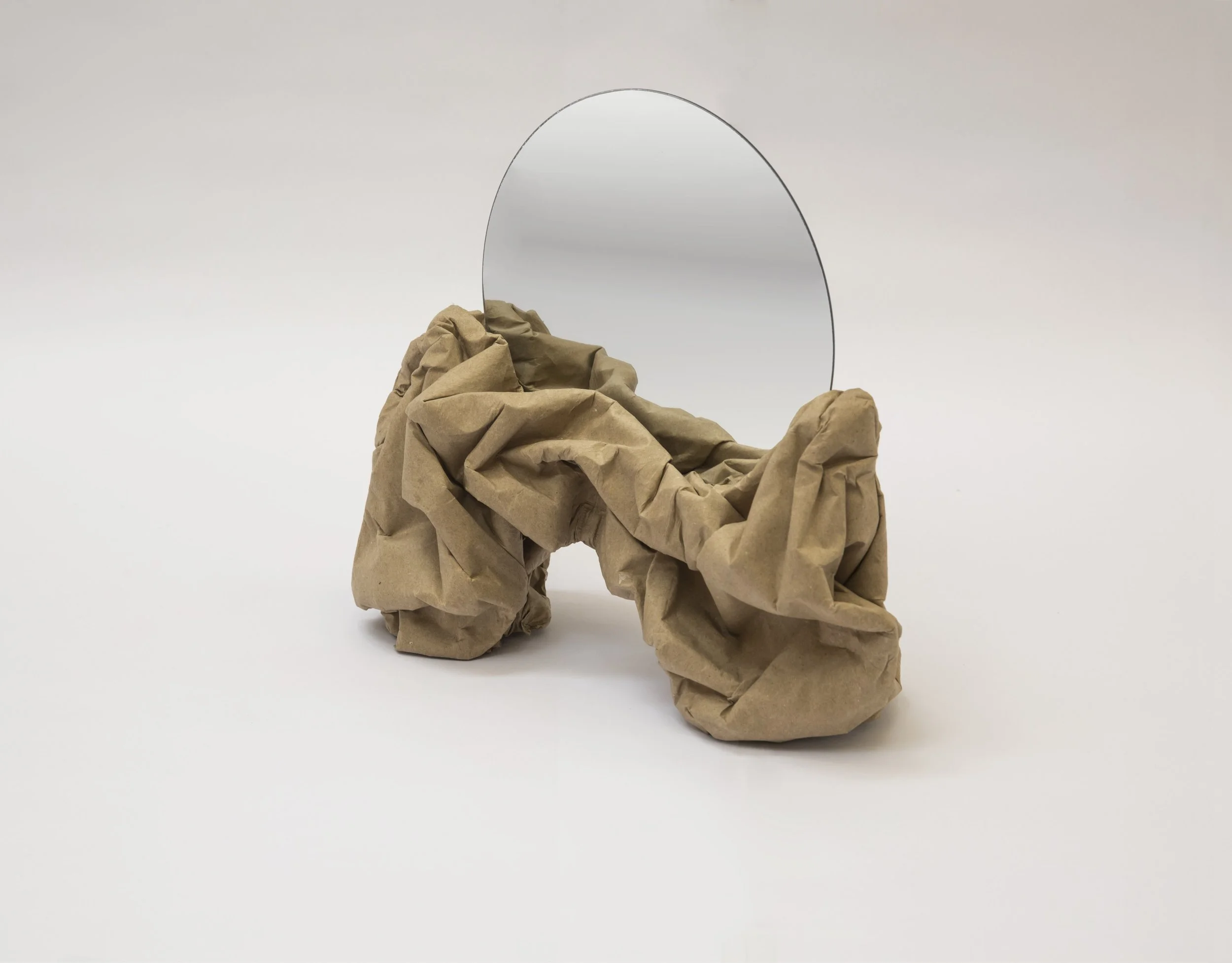 A mirror standing behind crumpled brown paper resembling a mountain, on a plain white background.
