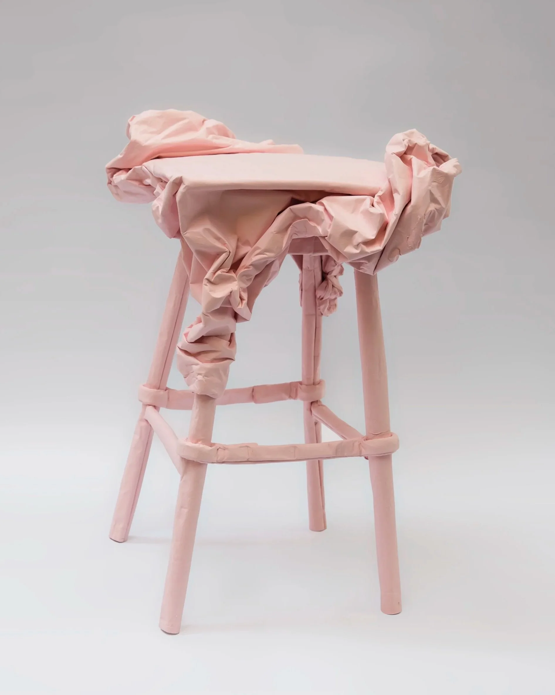 Pink wooden chair draped with pink fabric or plastic material, arranged to resemble a dress or clothing on the chair.