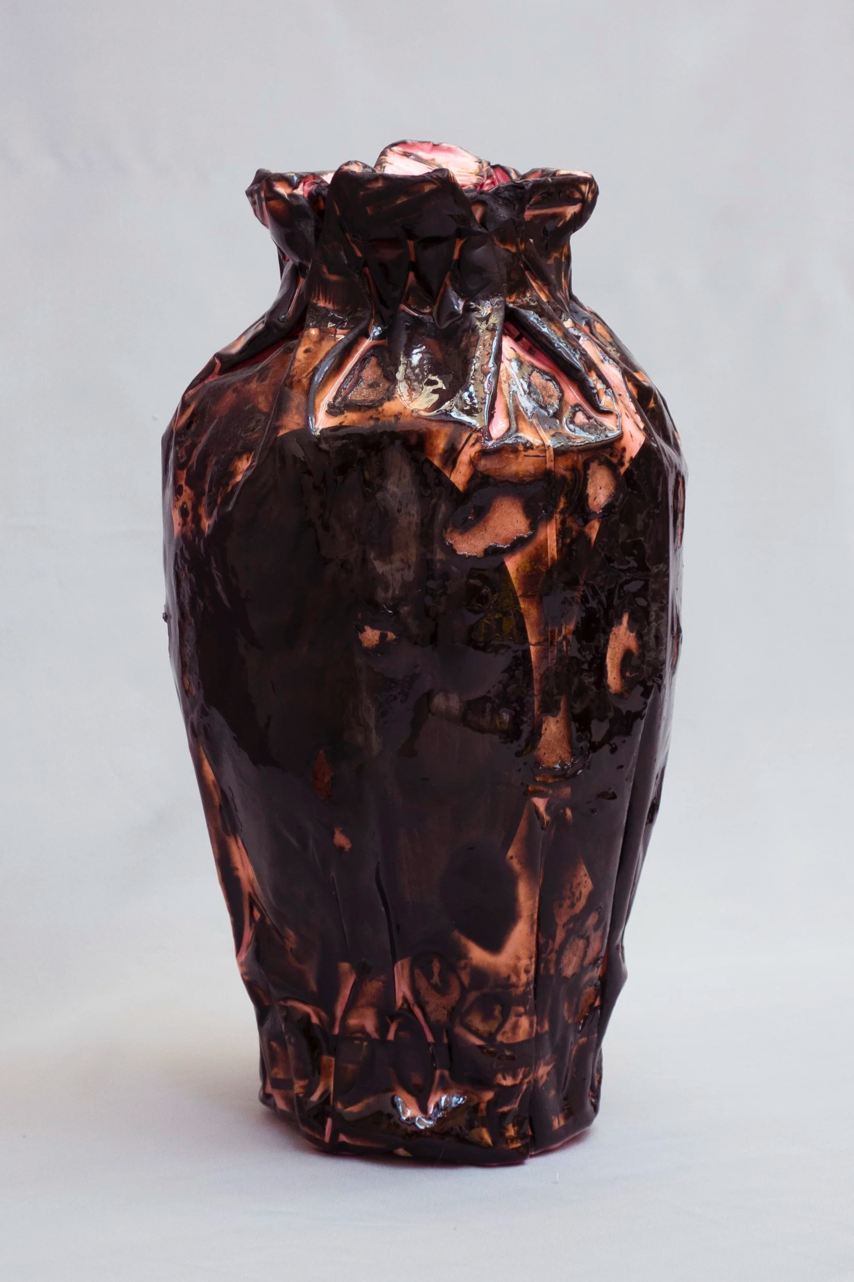 A sculpture resembling a wrinkled, crumpled metal or foil material, painted in dark, rusty colors with hints of pinkish hues.