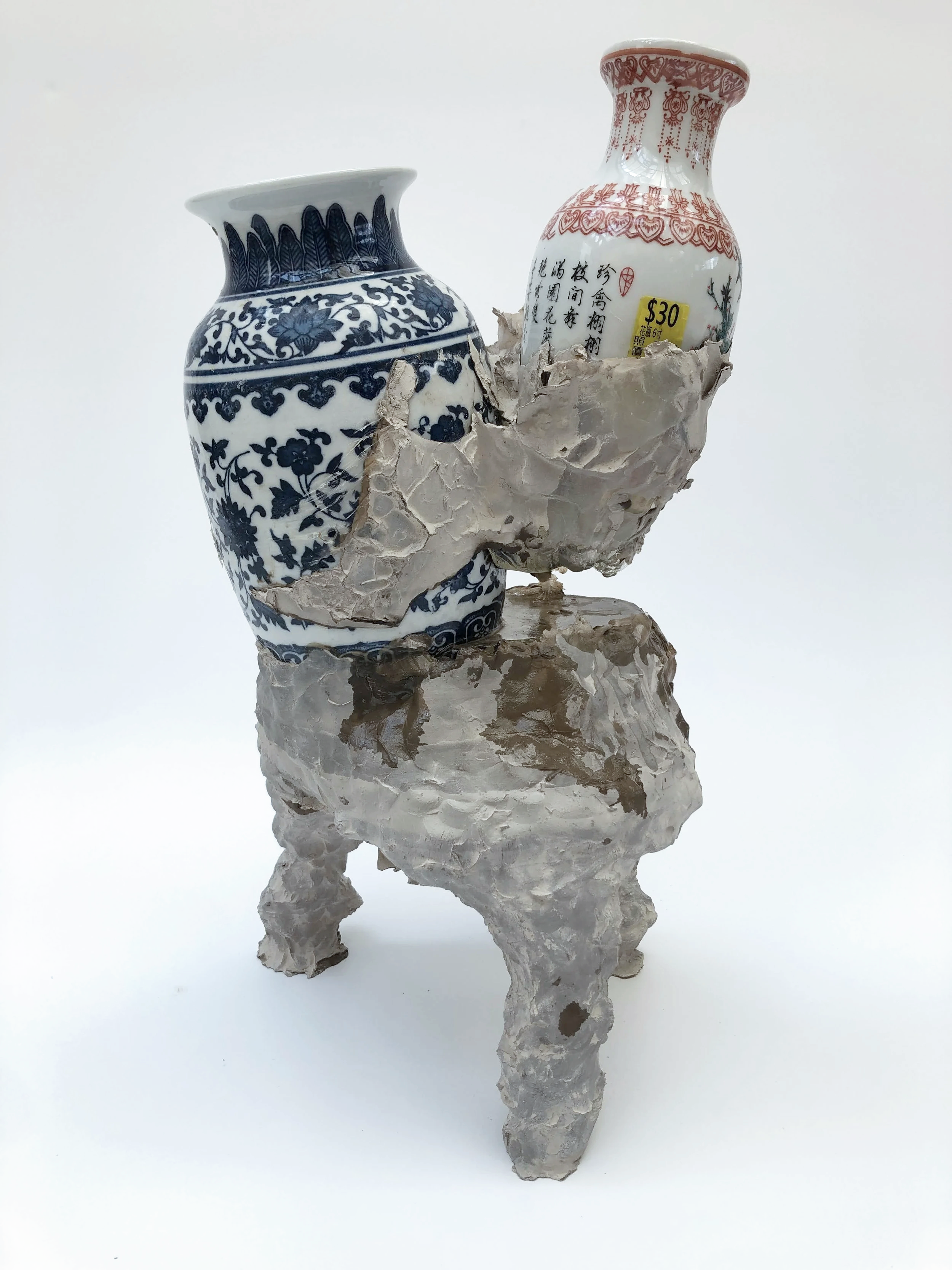 Decorative ceramic vases placed on an irregular stone pedestal with a white background.
