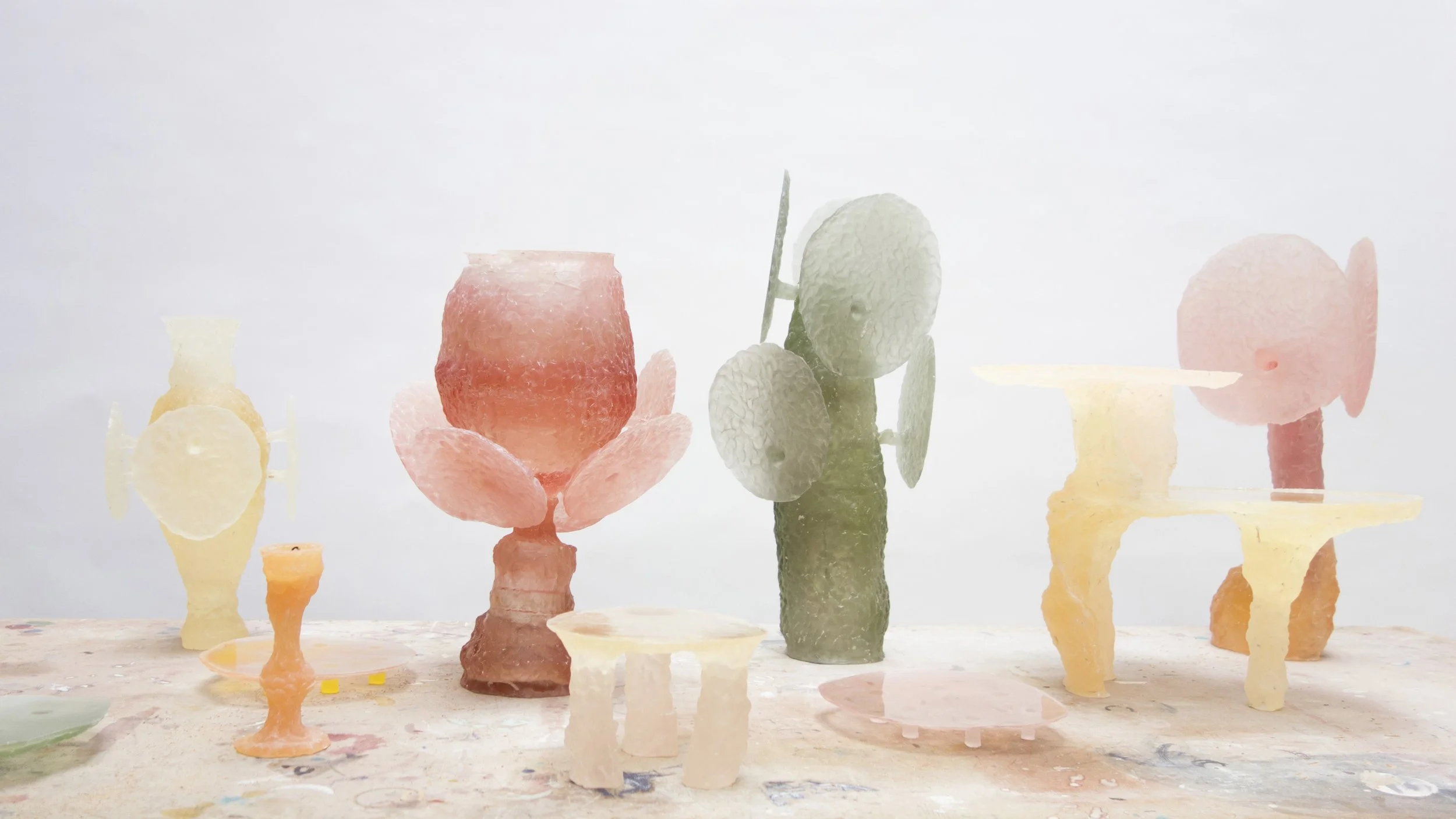 Colorful abstract sculptures resembling vases, flowers, and geometric shapes arranged on a table against a plain white background.