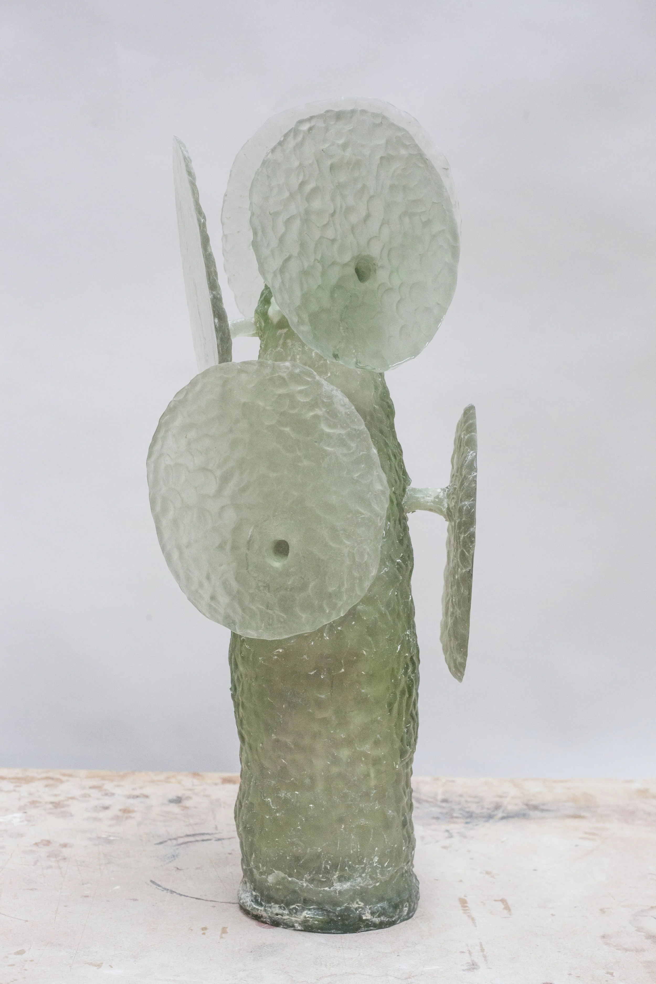 A sculpture made of textured, semi-transparent glass resembling a figure holding three circular shields.