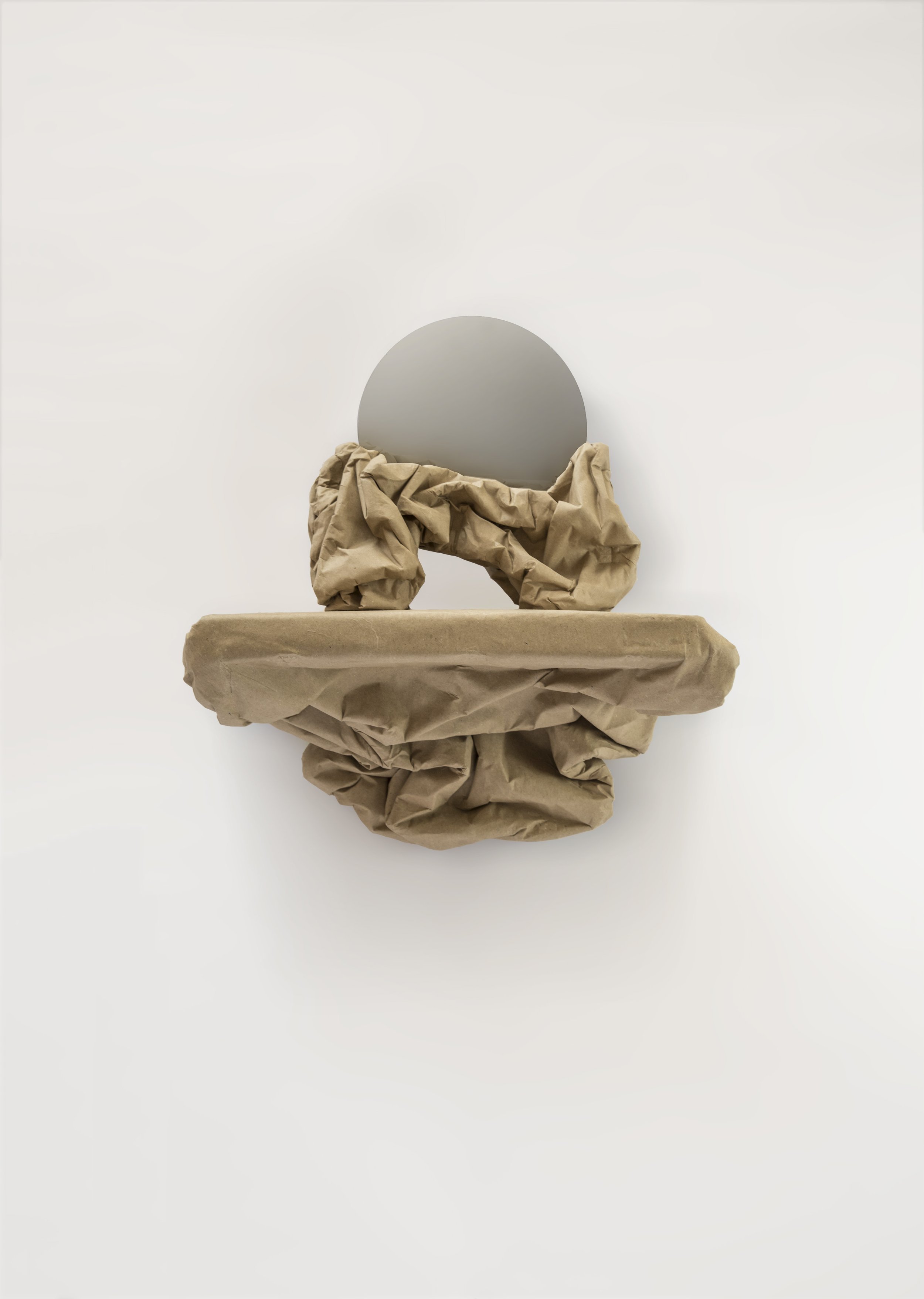 Abstract art piece with crumpled brown paper and a circular mirror on a white background.
