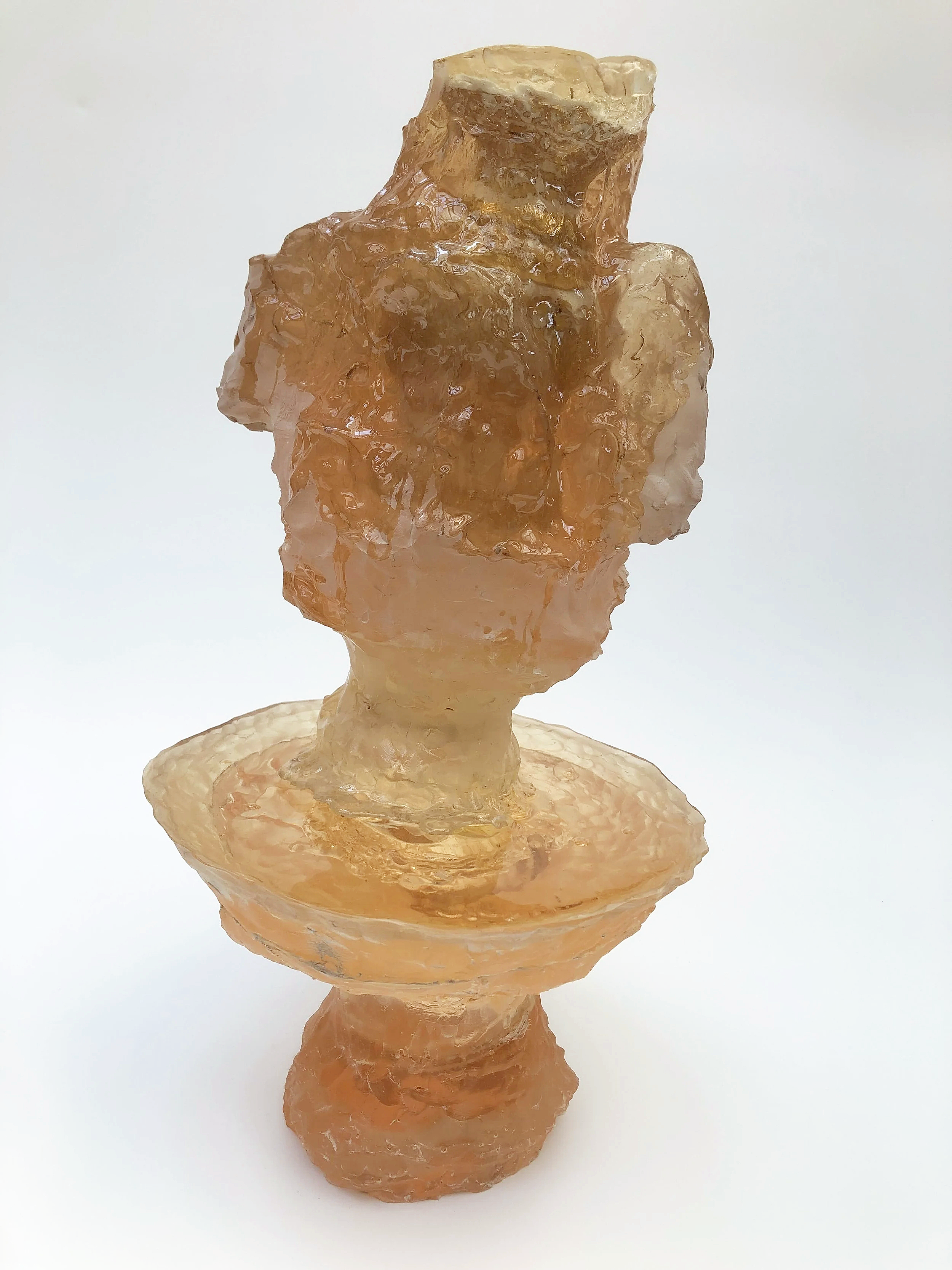 A sculpture of a human bust made from translucent, amber-colored salt blocks, positioned on a salt pedestal against a plain white background.