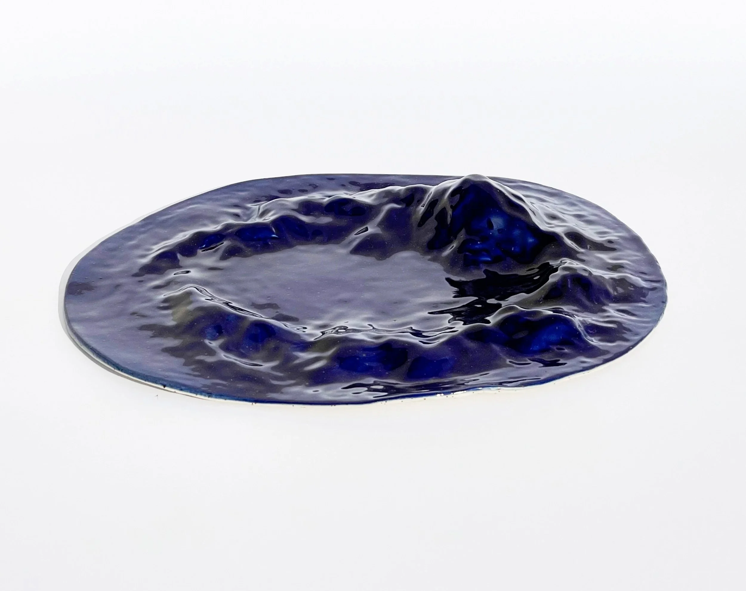 A dark blue, irregularly shaped, crumpled object resembling a melted or crinkled material, placed on a plain white background.