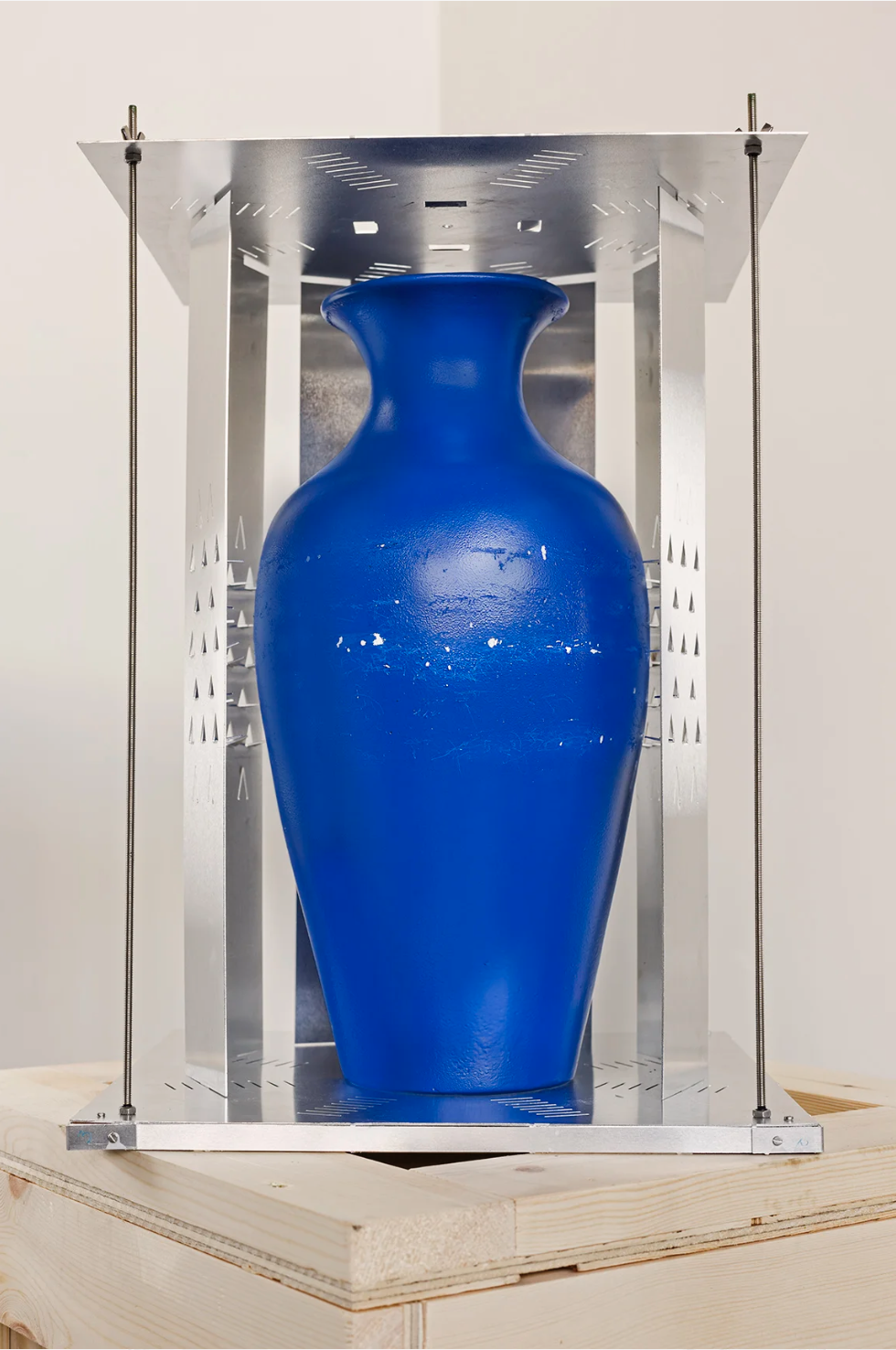 A large blue ceramic vase inside a metallic display case with a wooden base.