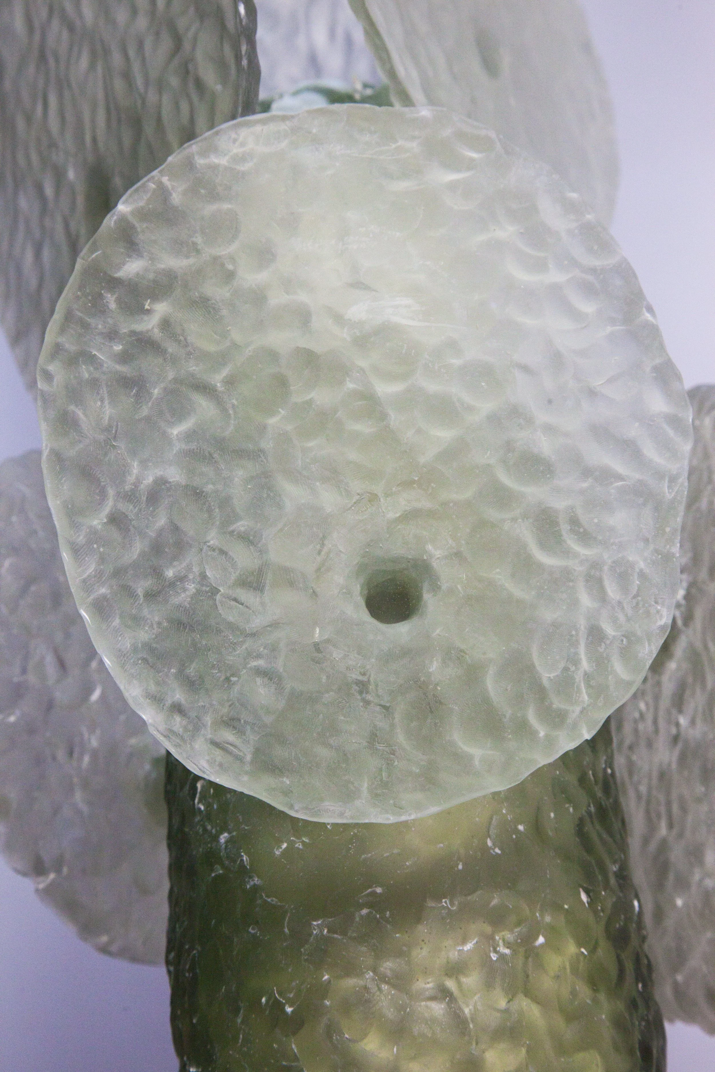 Close-up of a rough-textured, translucent ice disc with a small hole in the center, placed on a reflective surface with other ice pieces around.