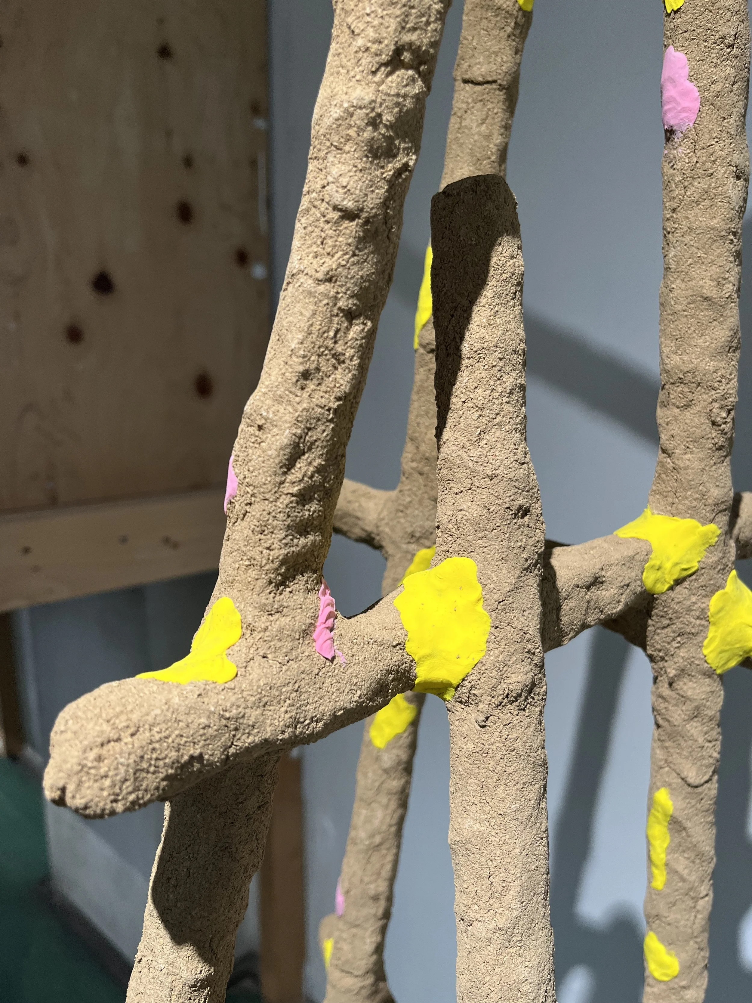 Close-up of a textured beige sculpture resembling a tree with pink and yellow paint accents.
