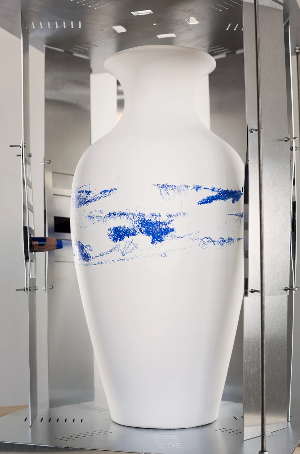 A white ceramic vase with blue abstract markings, displayed within a metallic display case.