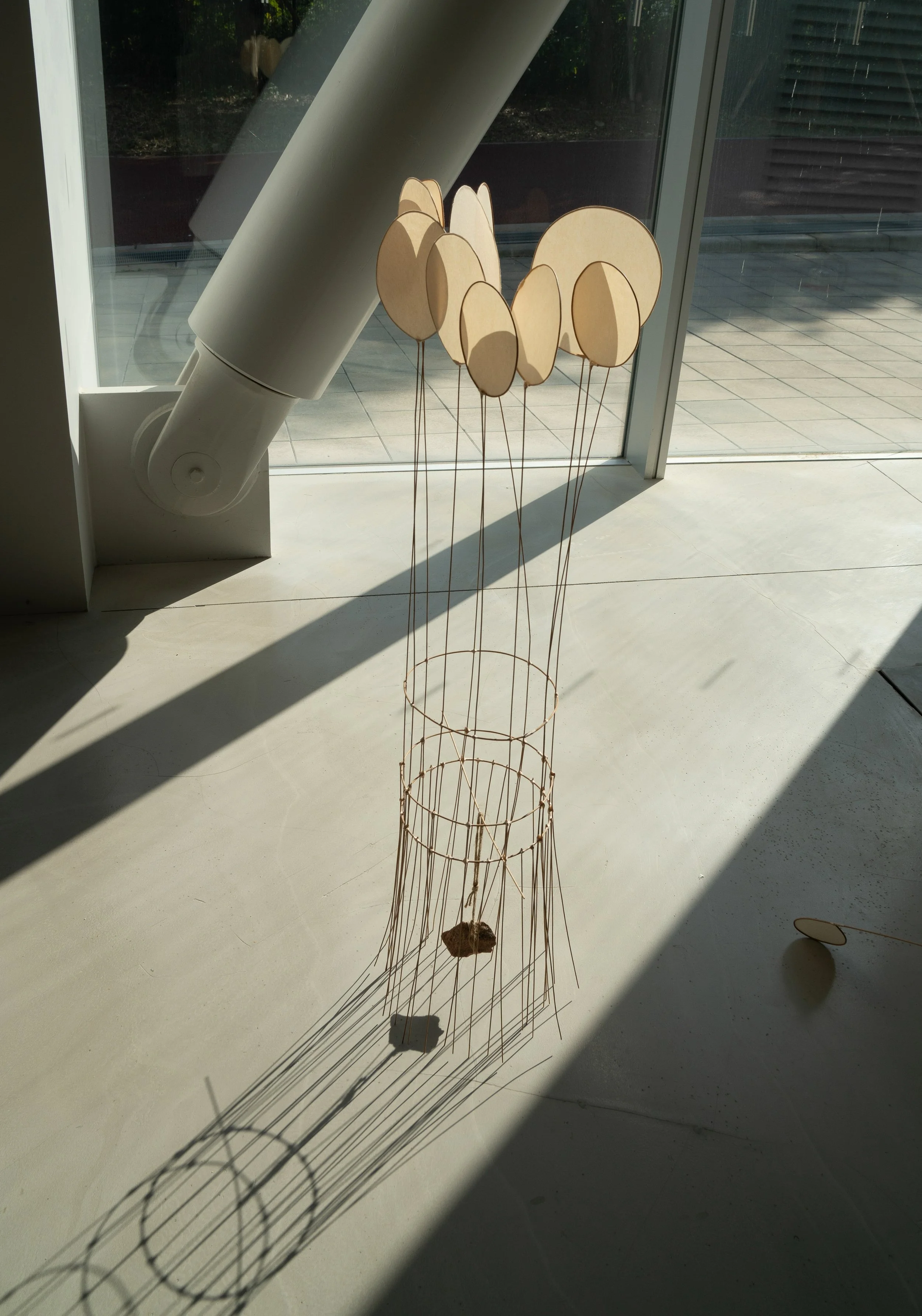 A modern art sculpture resembling balloons or bubbles is placed in front of a large glass window, casting shadows on the floor.