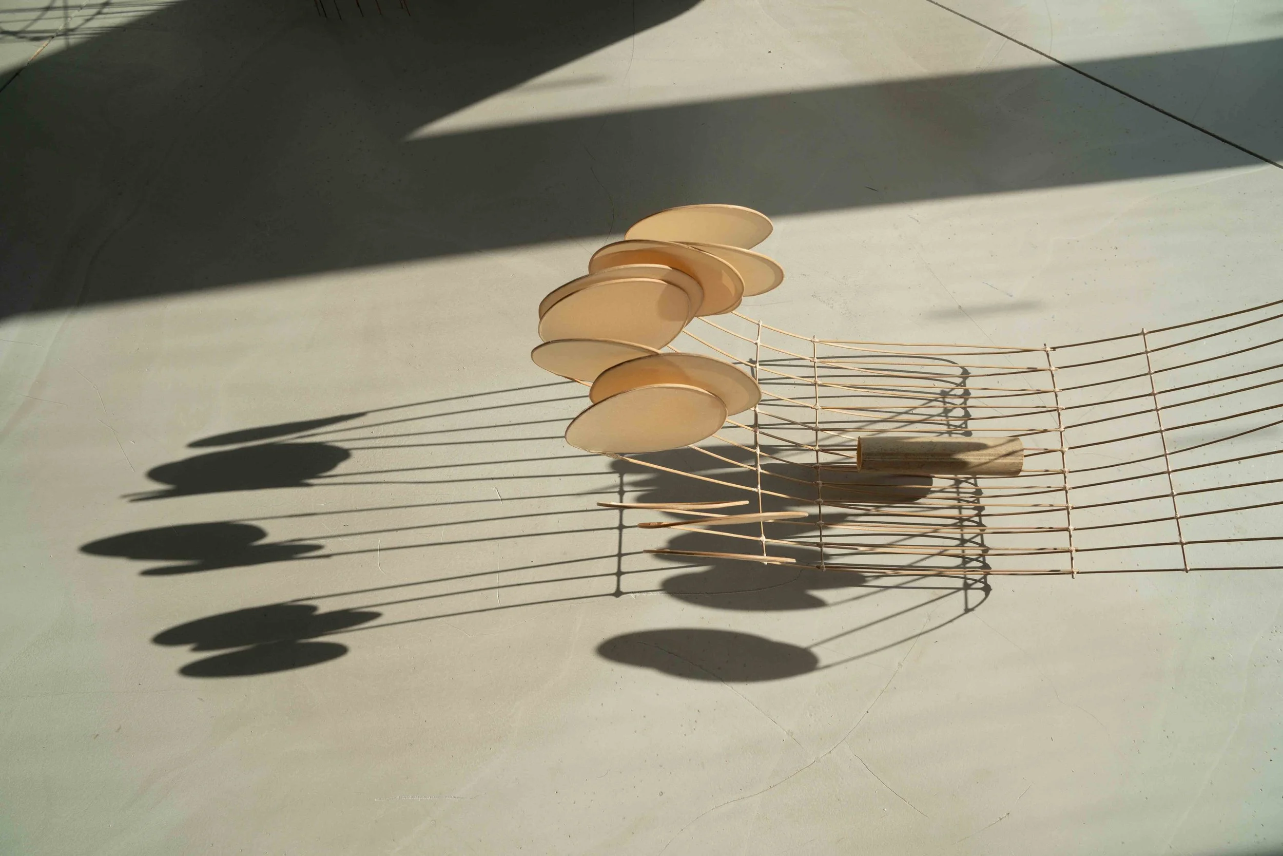 A modern decorative wind chime with beige circular discs hanging from thin wires, casting shadows on a light-colored surface.