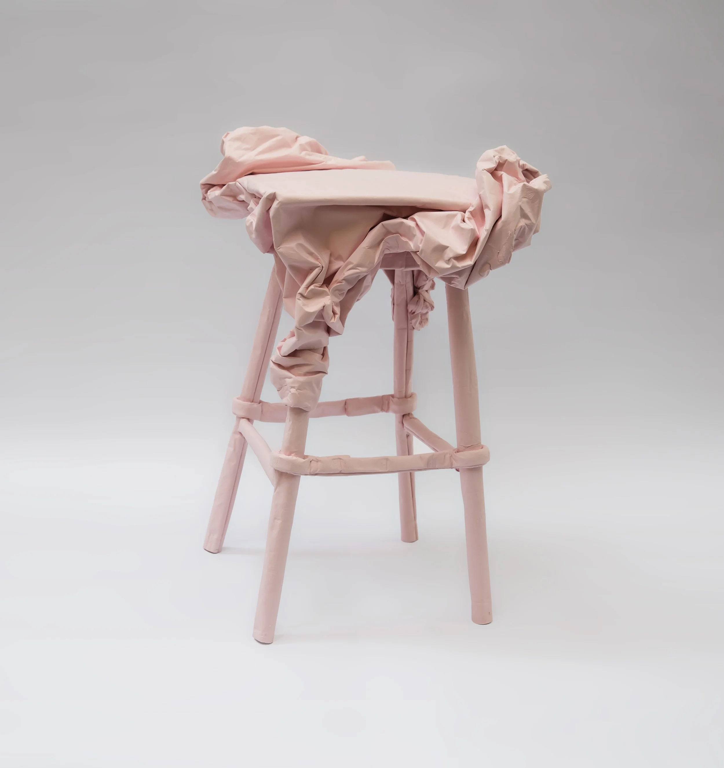 A pink high chair with a crumpled pink fabric draped over the seat, set against a plain light gray background.