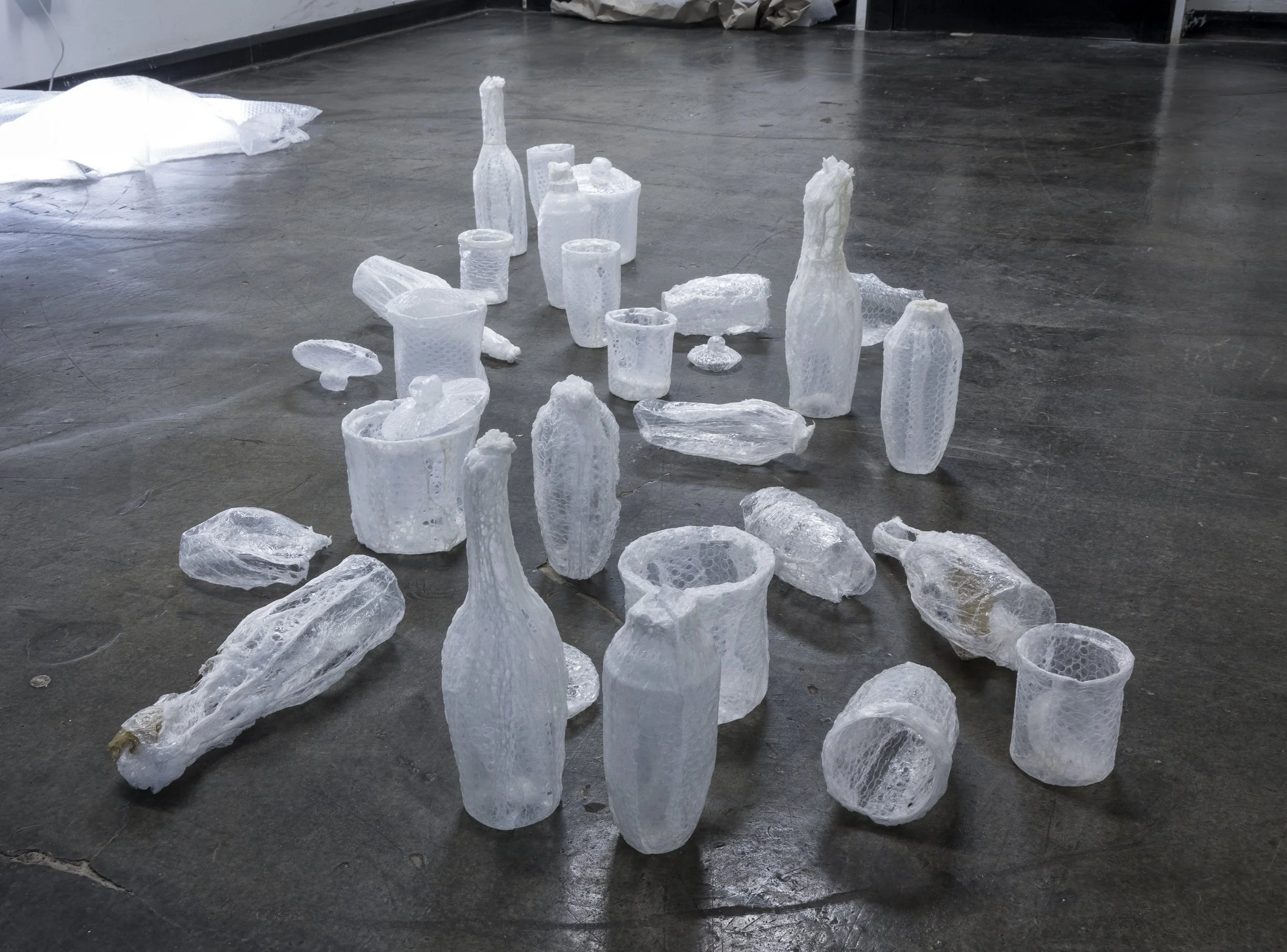 Various empty glass bottles and cups covered in bubble wrap, arranged on a warehouse floor.