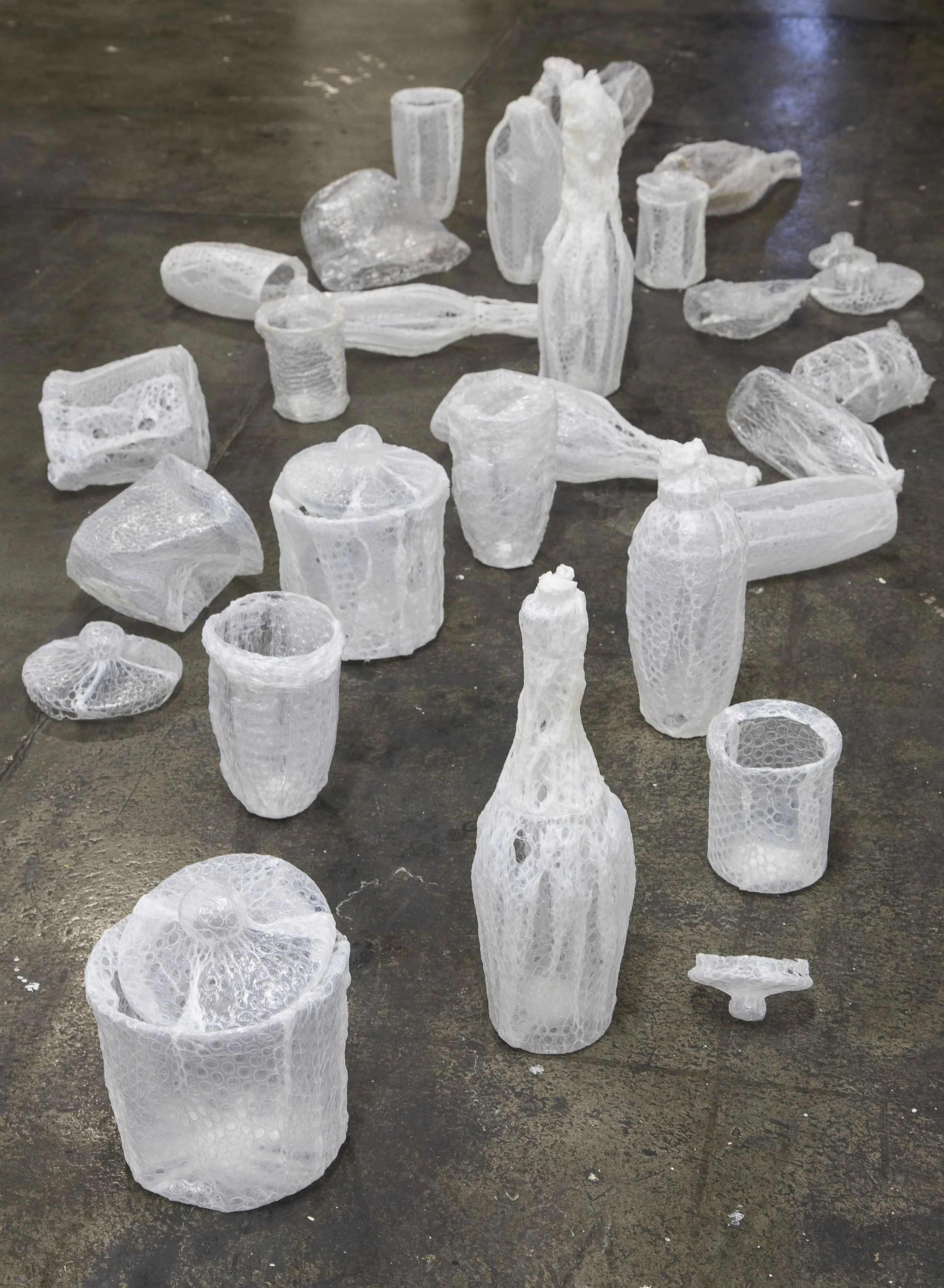 Collection of clear plastic bubble wrap vases and bottles on a dark floor.