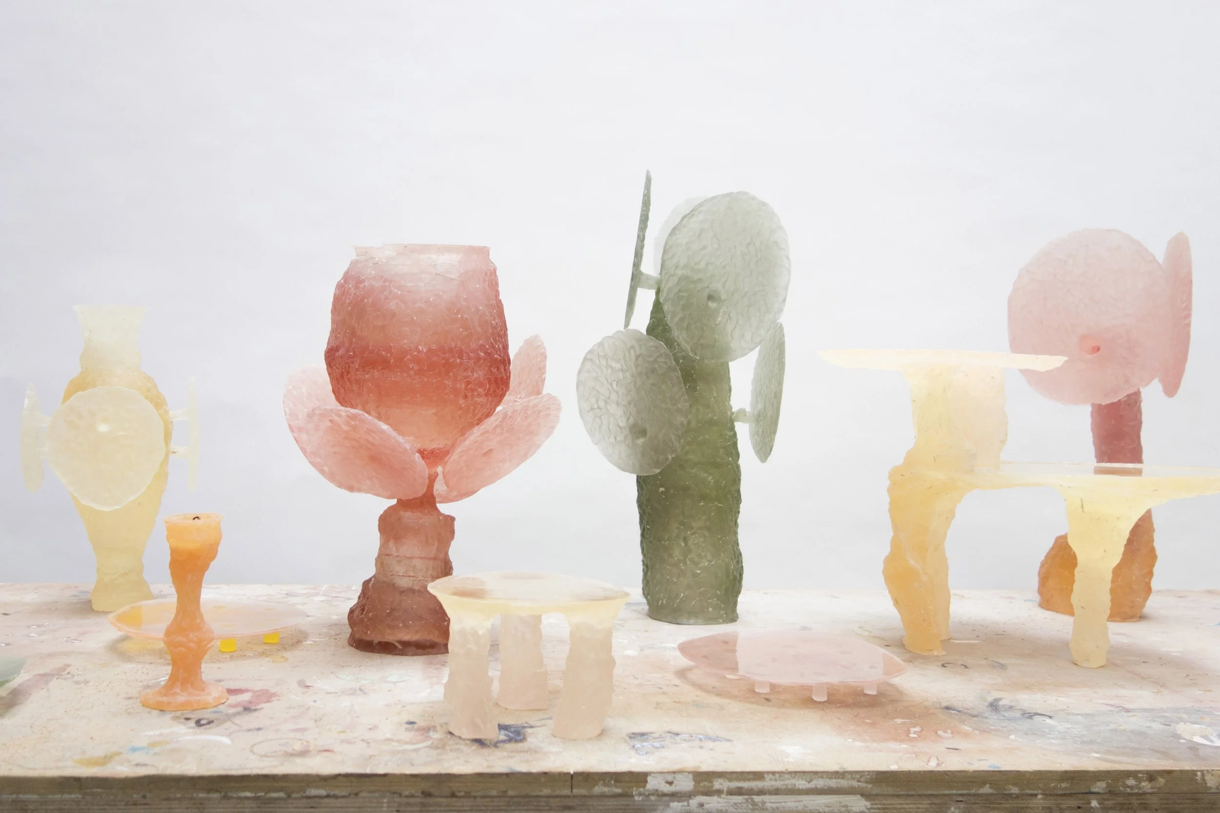 Assorted pastel-colored salt or wax sculptures resembling various geometric and abstract shapes, including vases, platters, and decorative objects on a wooden table against a plain white background.