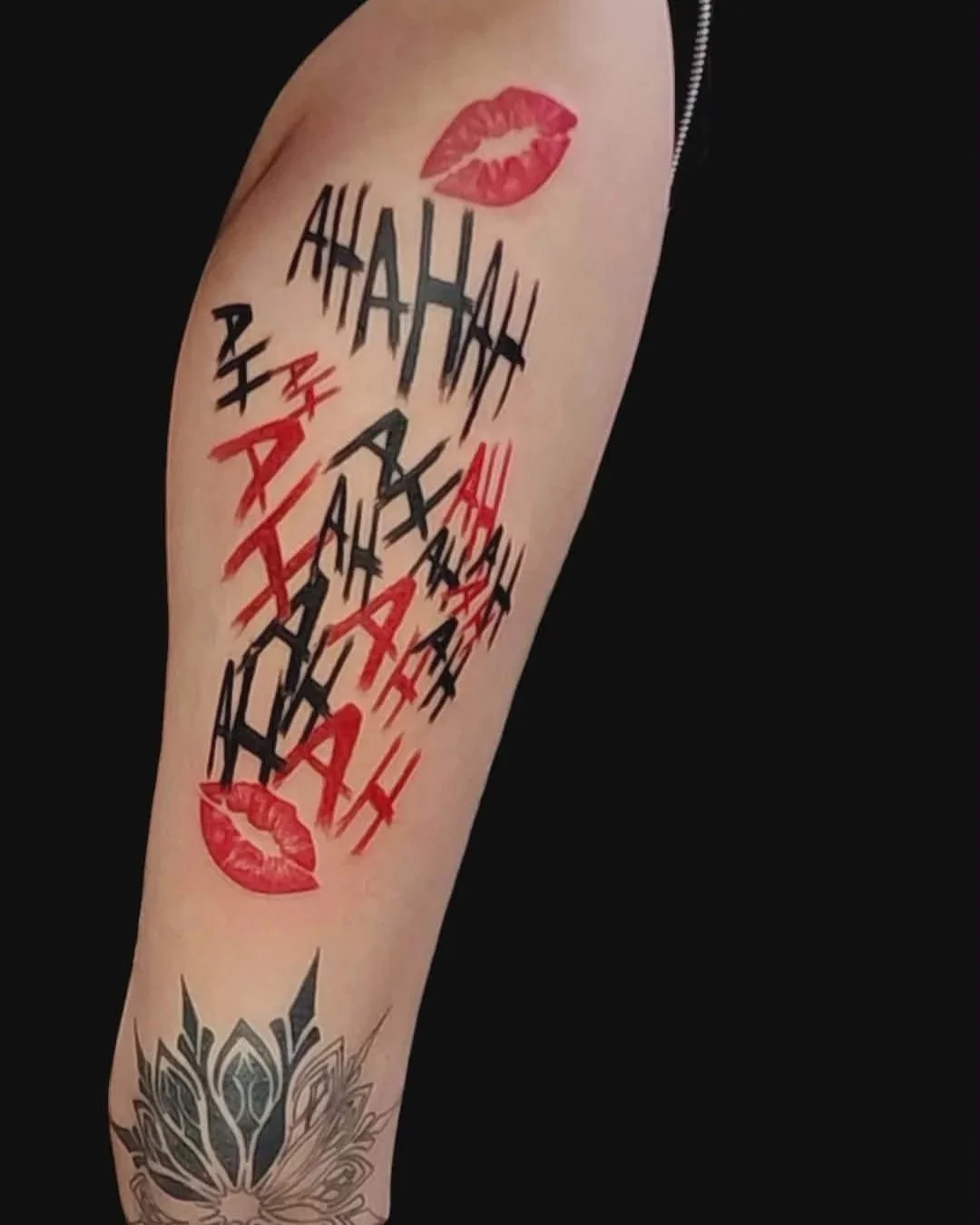 Tattoo on arm featuring red lipstick kisses and the phrase 'AHAHAHA' in black and red stylized text.