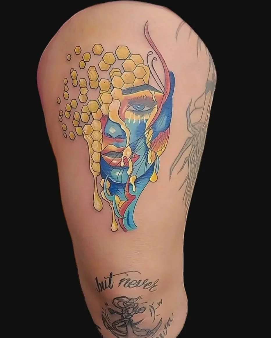 Tattoo of a woman's face with colorful abstract and geometric elements, including honeycomb shapes and flowing lines, on an arm.