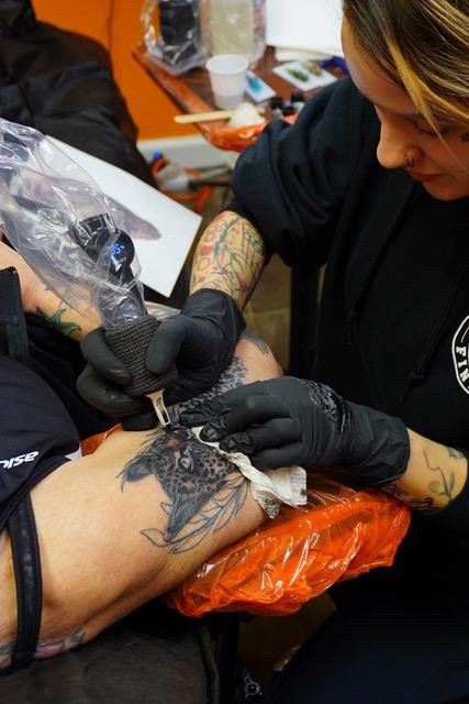 Tattoo artist working on a person's leg in a tattoo studio.